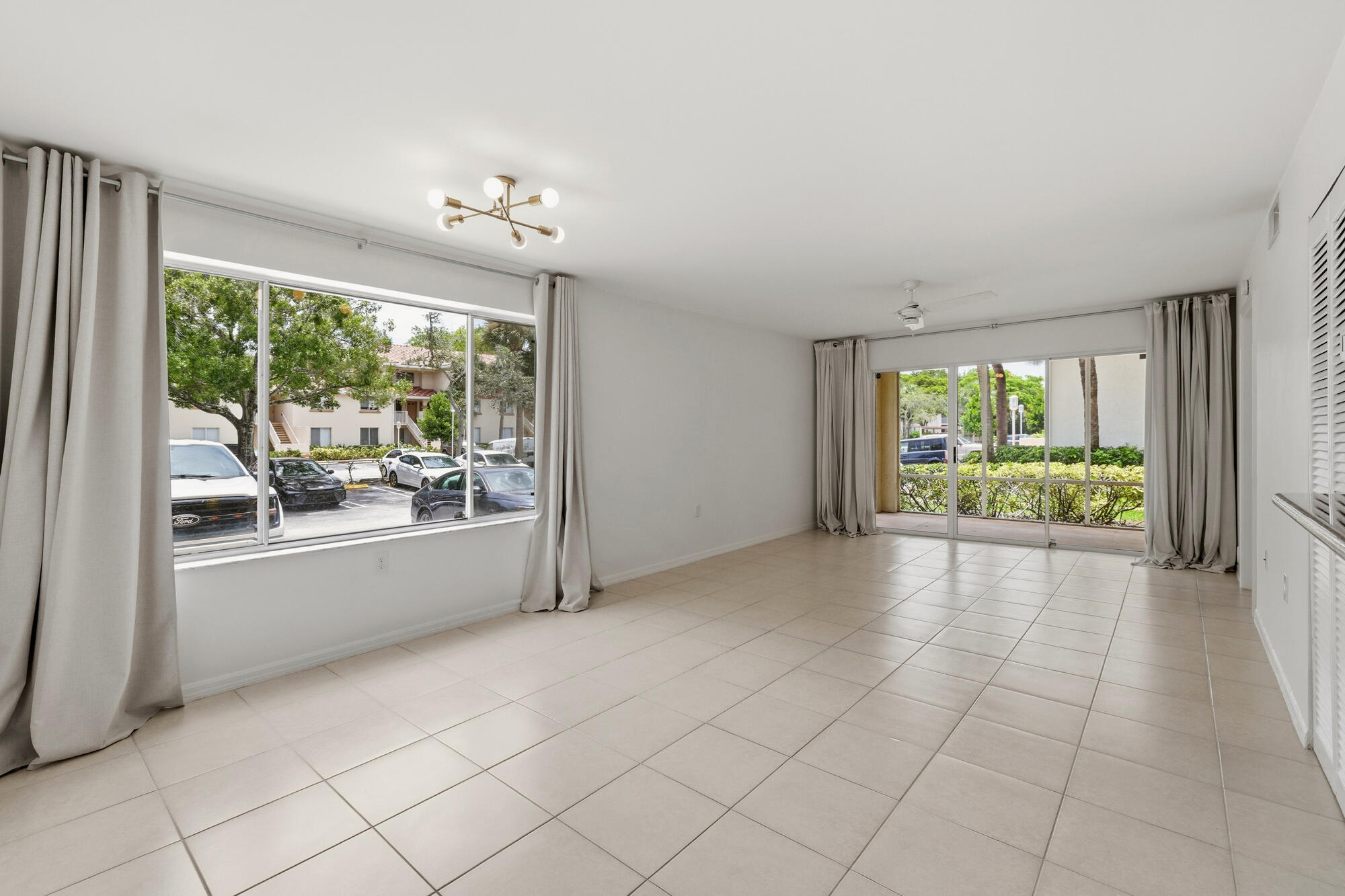 Spacious living area featuring neutral tile flooring, a wide window with light-filtering drapes, and a contemporary ceiling fixture