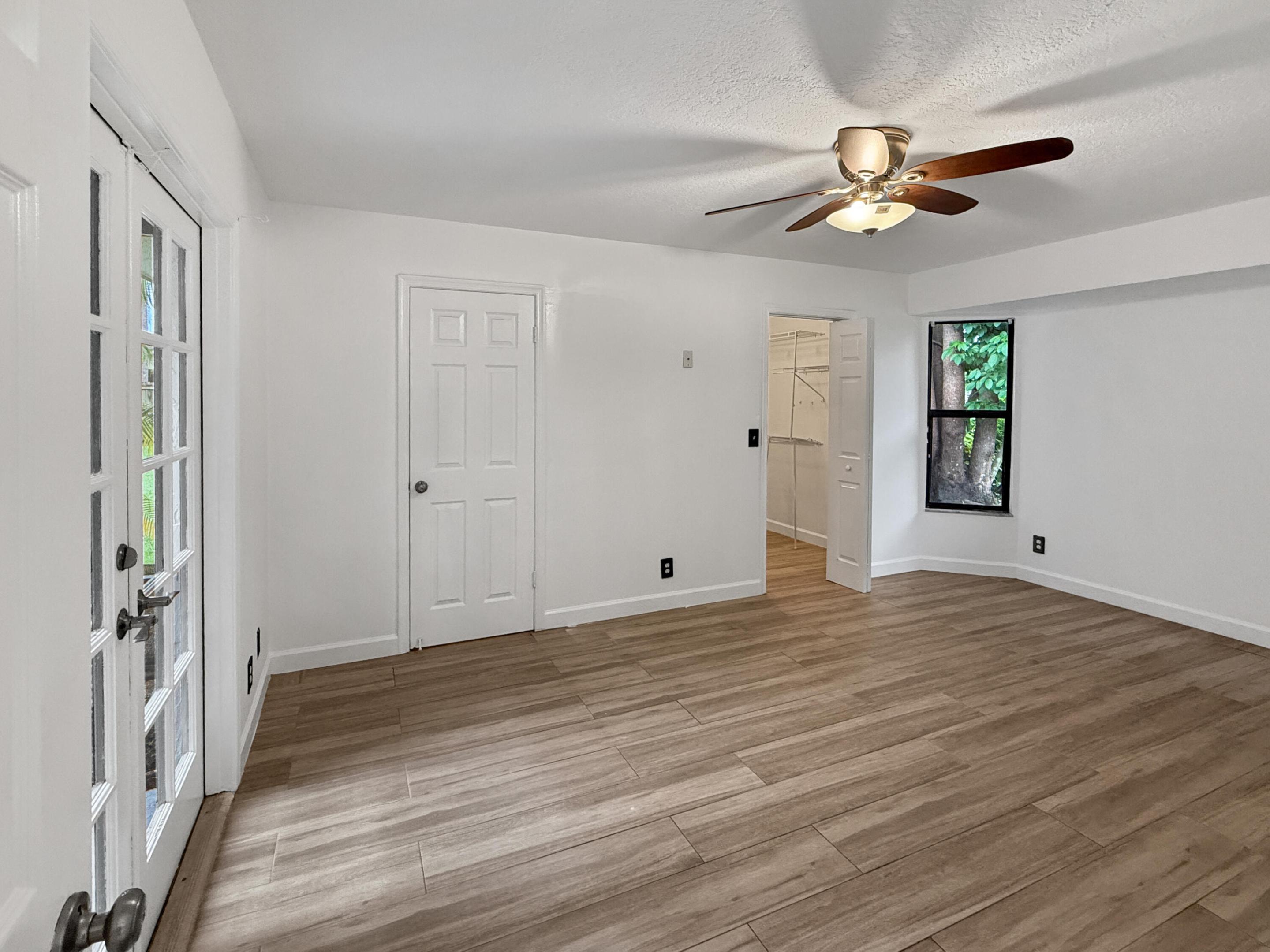 Wood-finish tile flooring, white walls, ceiling fan, French doors, and an additional doorway