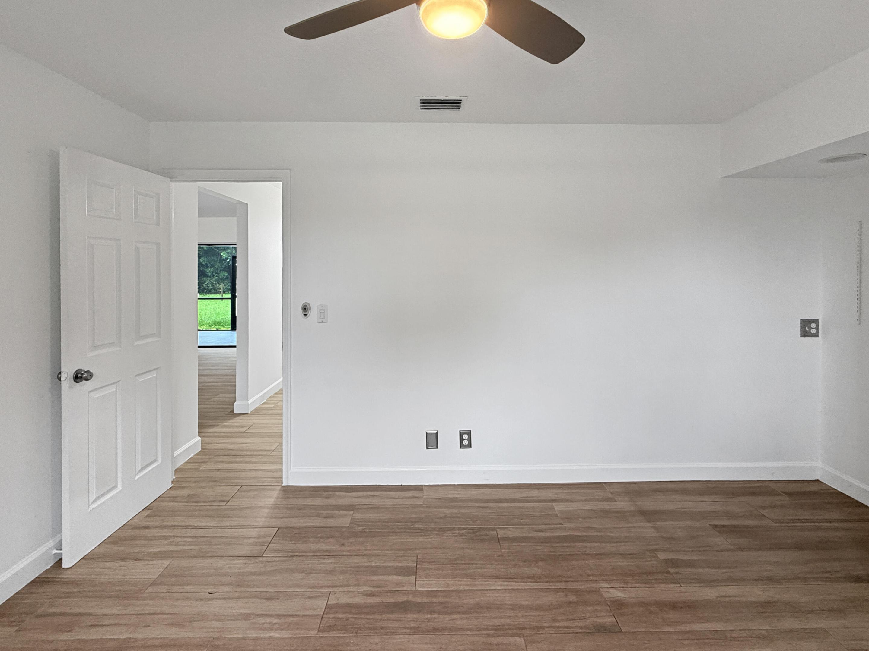 Wood-finish flooring throughout, white interior walls, and a ceiling fan with integrated lighting