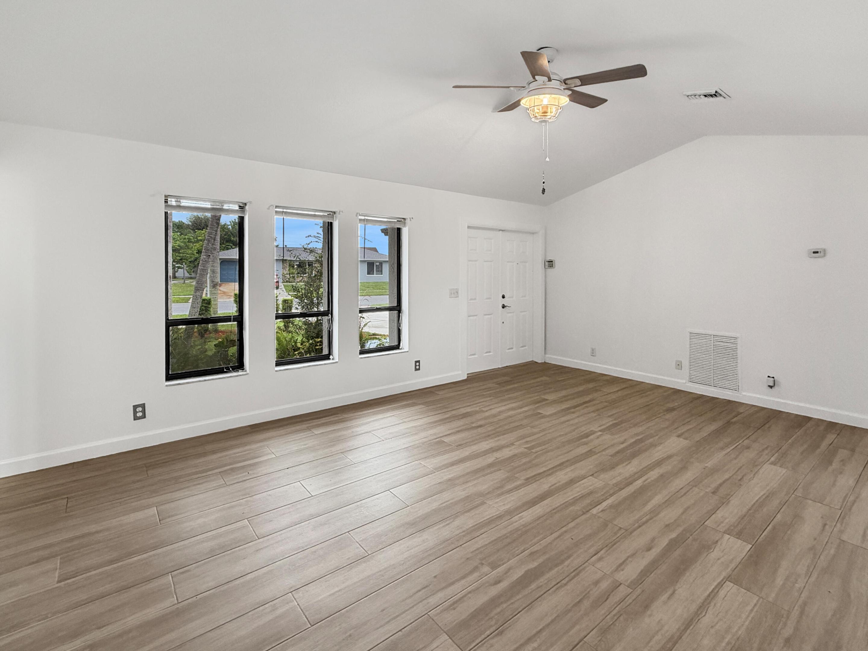 Vaulted ceilings, wood-finish flooring, three large windows, and a ceiling fan with light fixture