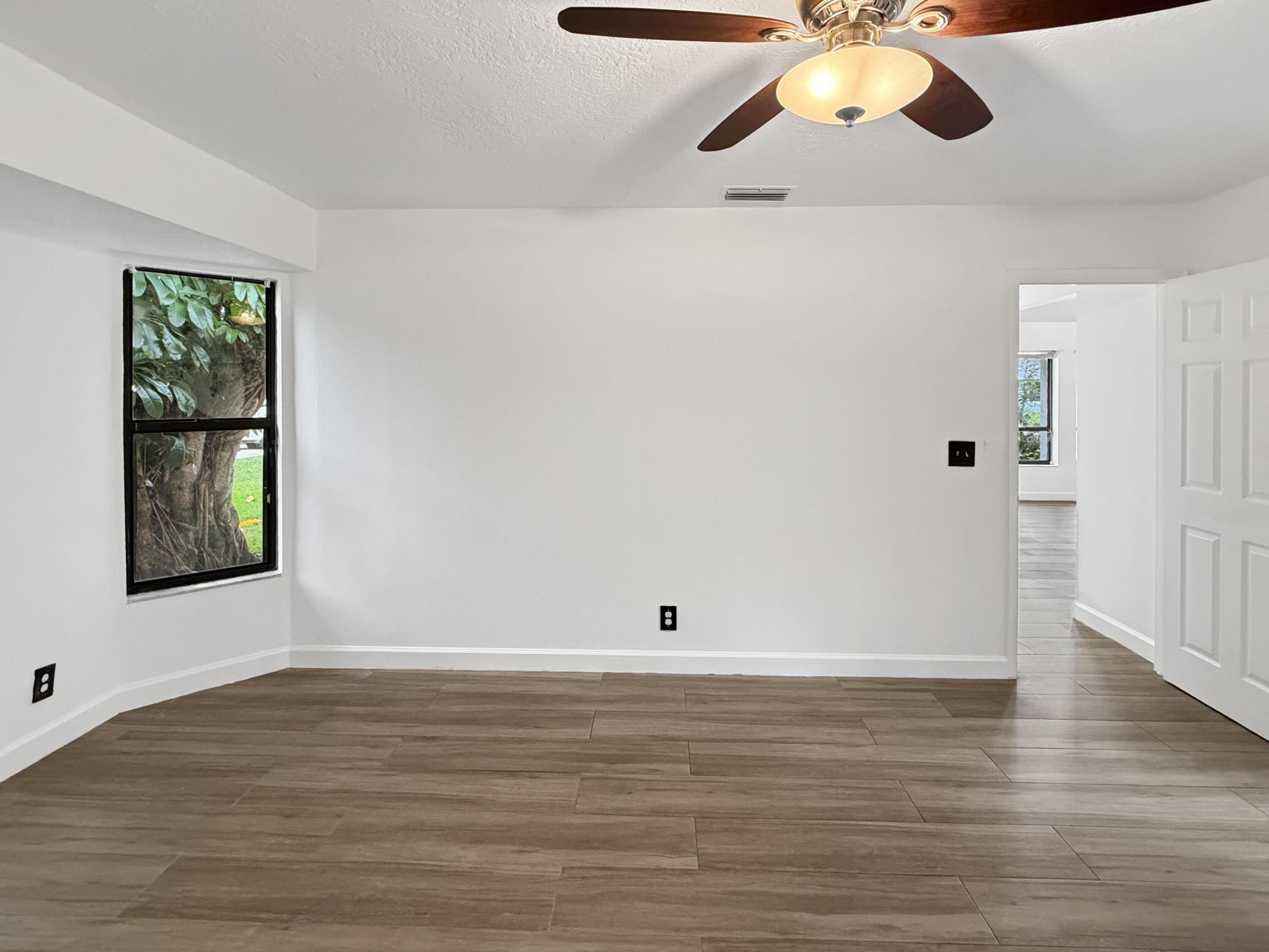 Wood-finish tile flooring, white painted walls, ceiling fan with integrated lighting, and a single window with exterior scenery