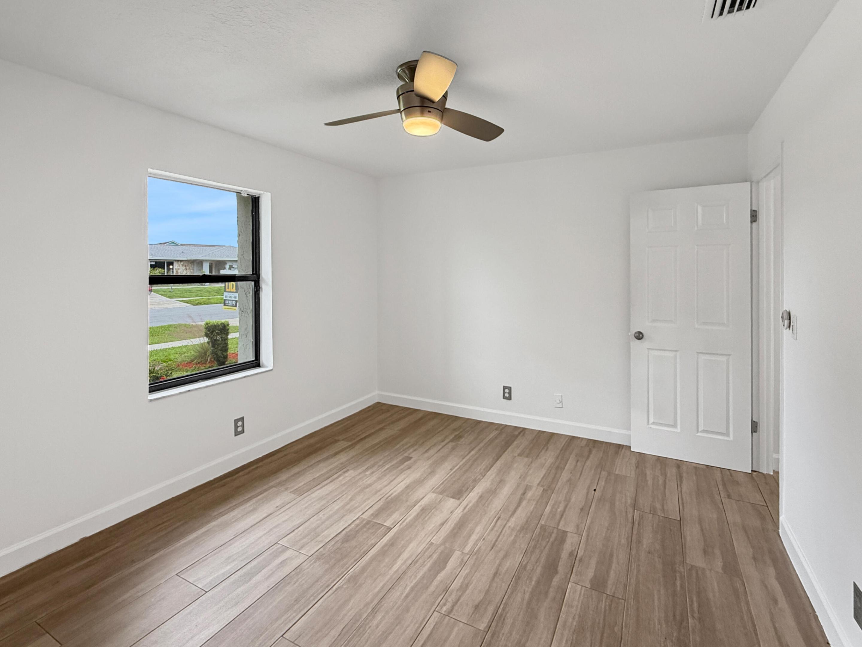 Bright corner bedroom featuring wood-finish flooring, a ceiling fan with integrated lighting, large window with natural light, and white six-panel closet door with chrome hardware