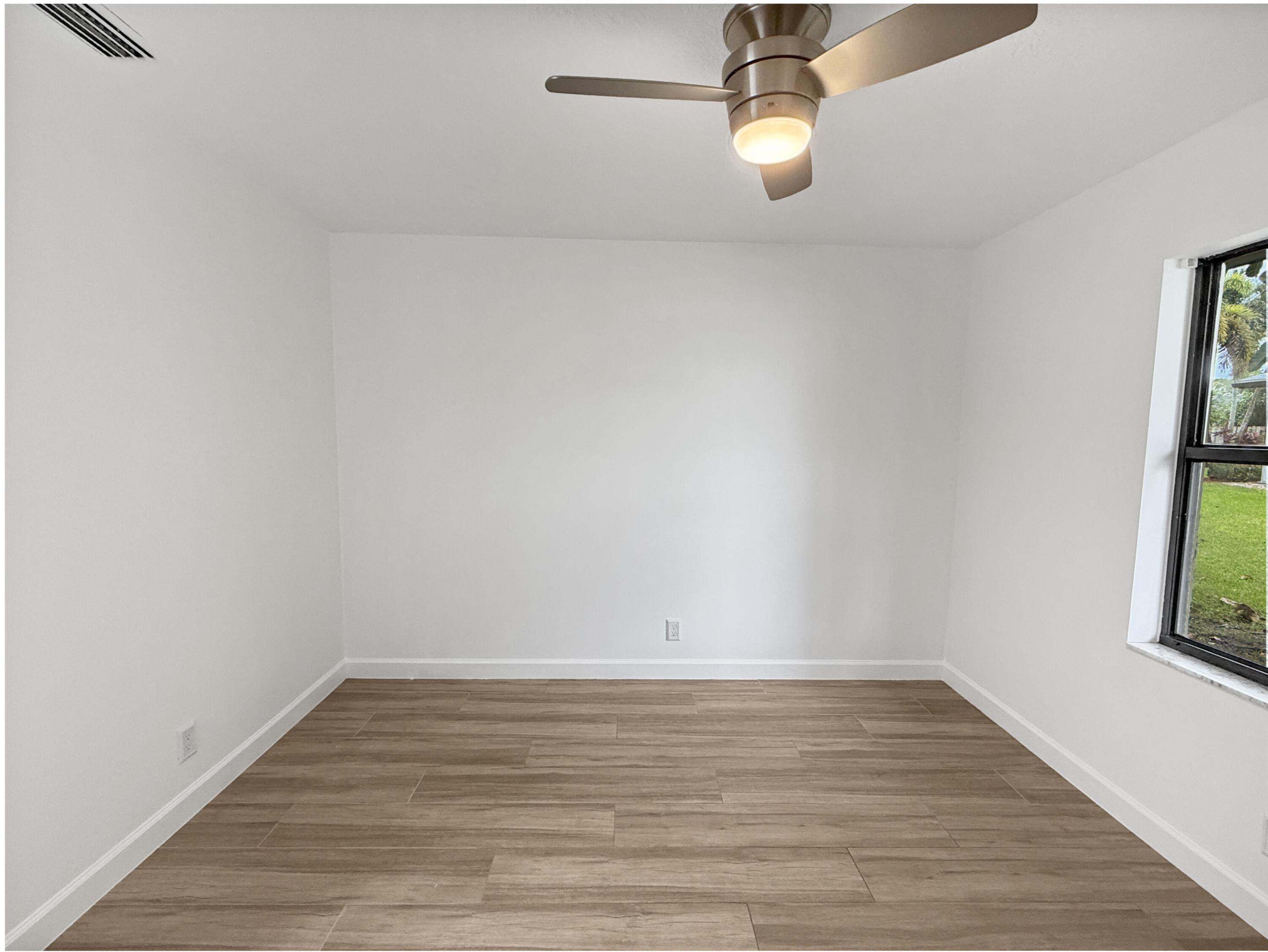 Wood-finish tile flooring, white painted walls, and a ceiling fan with integrated lighting