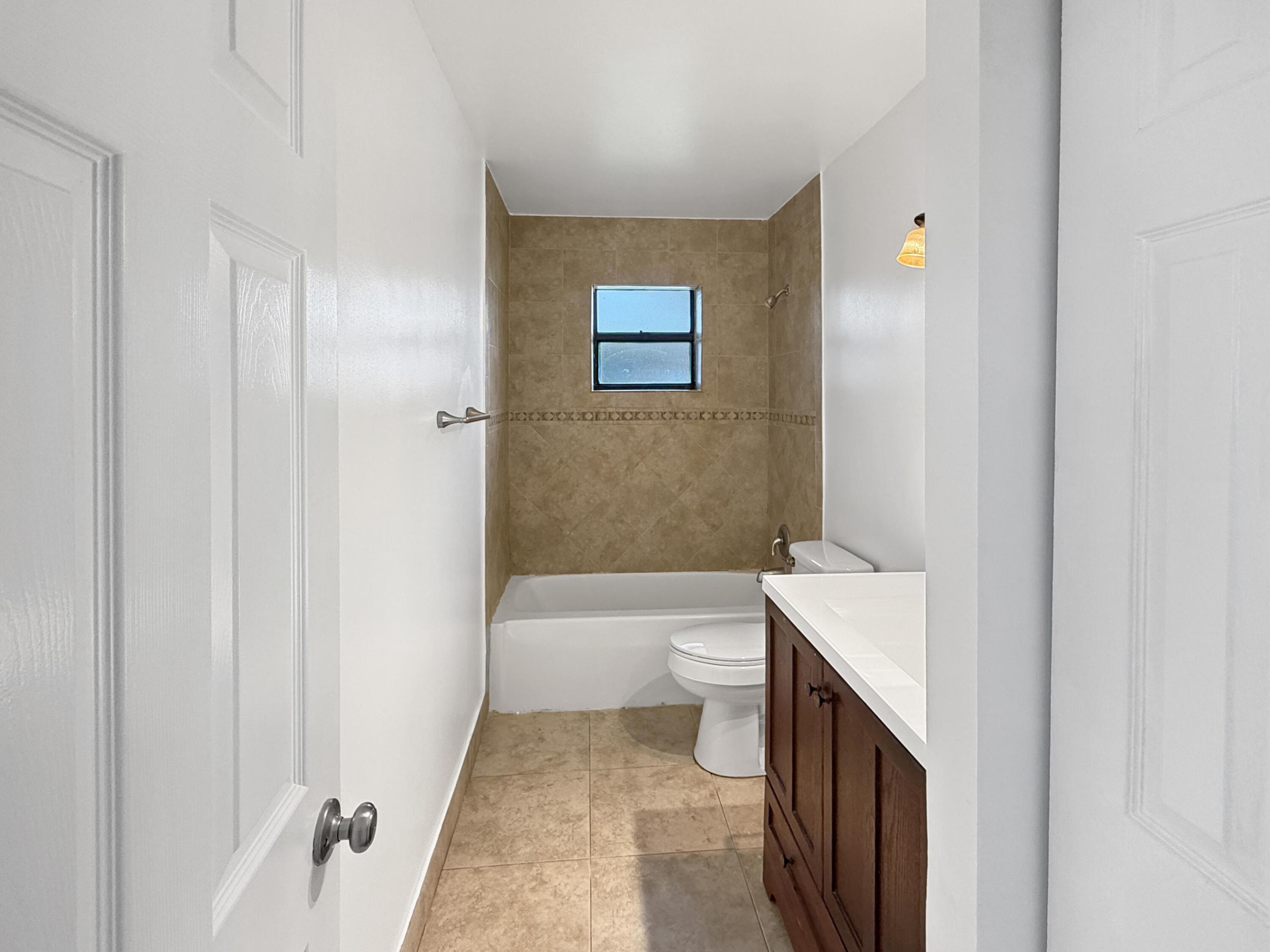 Tiled shower surround with decorative accent, built-in bathtub, and a window