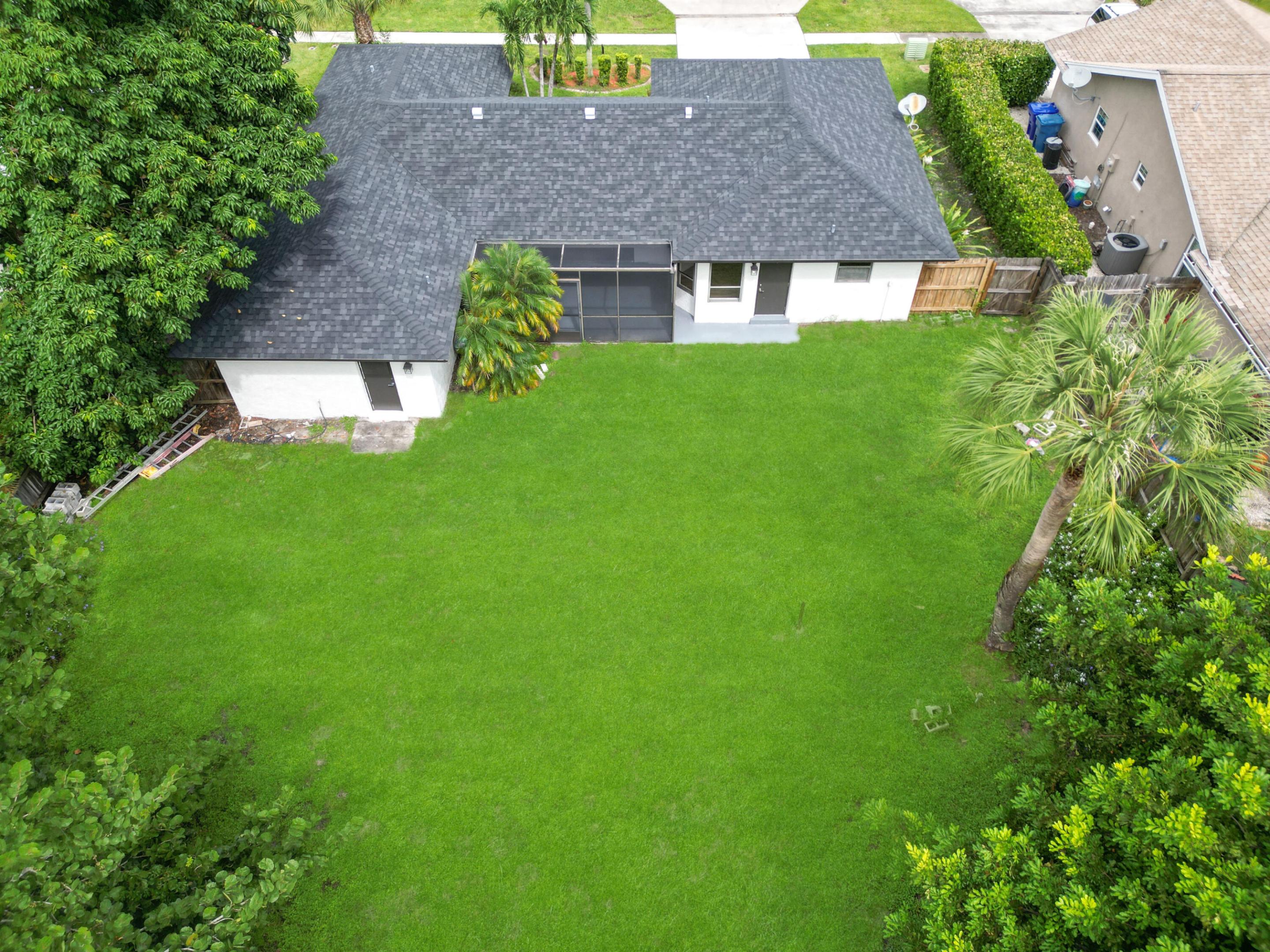 Expansive green lawn, dark shingle roof, mature trees, and privacy fencing