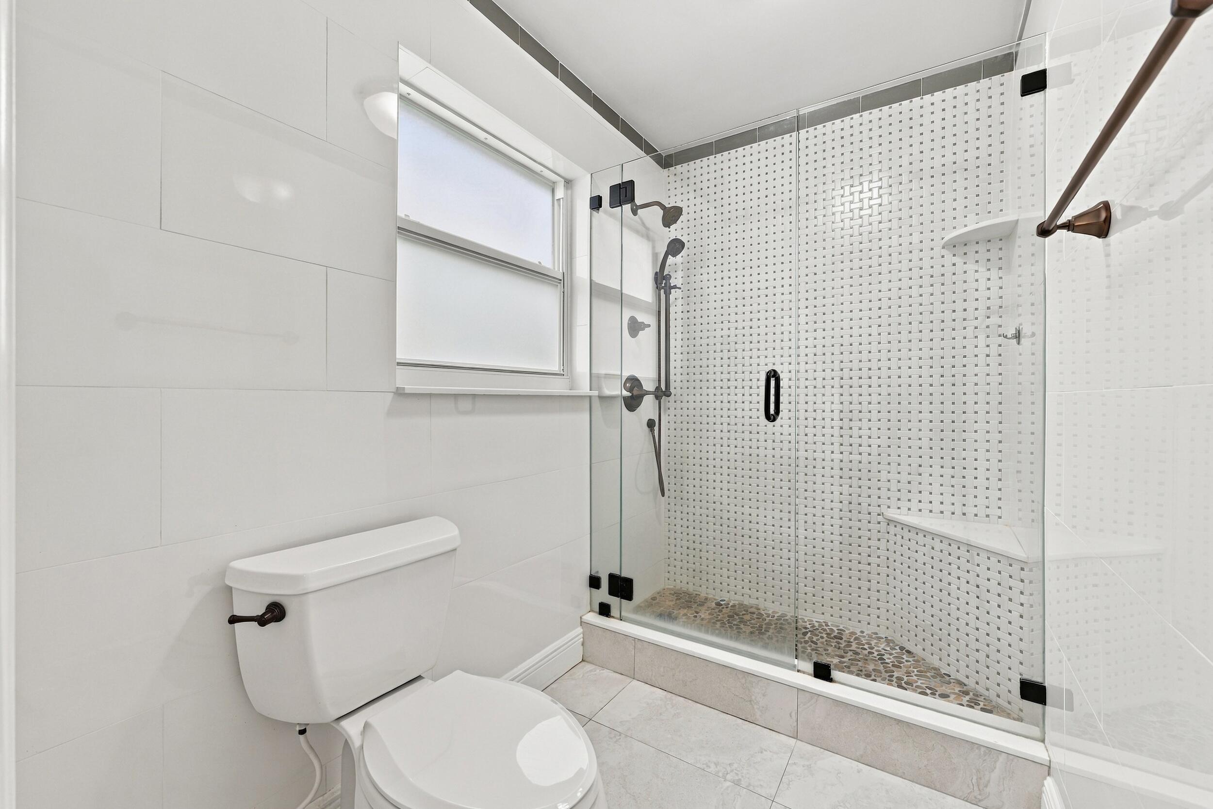 The fully renovated primary bathroom offers dual sinks, updated cabinetry, and a brand-new frameless glass shower.