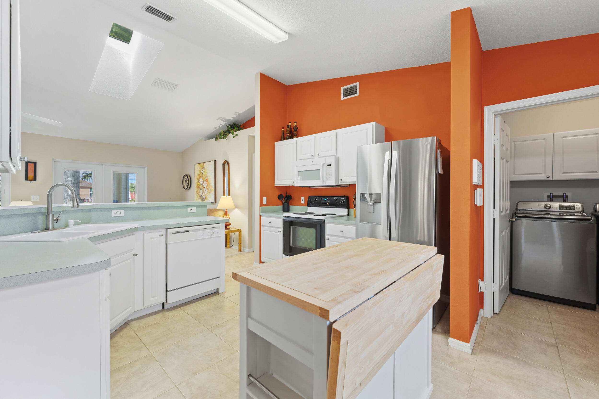 Kitchen featuring white cabinetry, stainless steel appliances, butcher-block top center island, tile flooring, and a skylight
