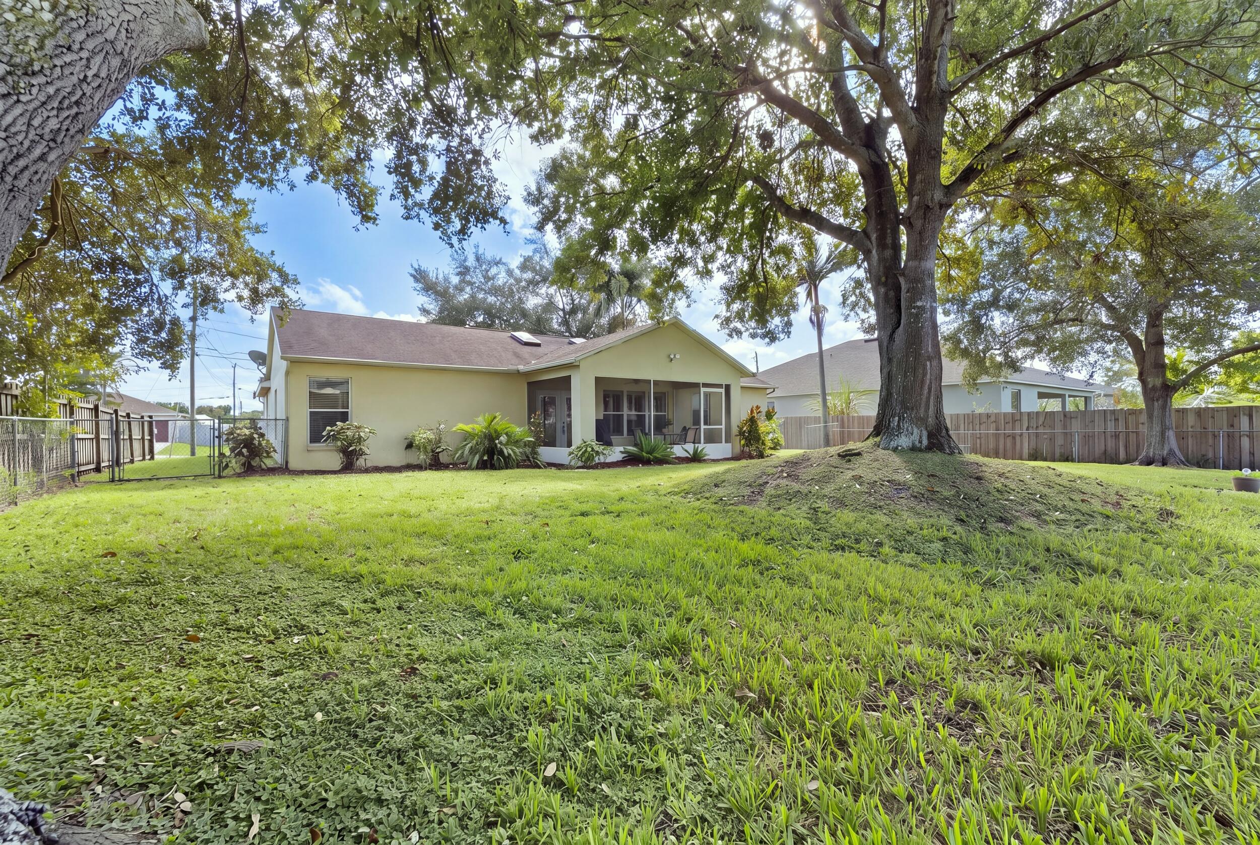 Expansive backyard featuring a large mature tree, manicured lawn, perimeter wood fencing, and a covered screened-in patio