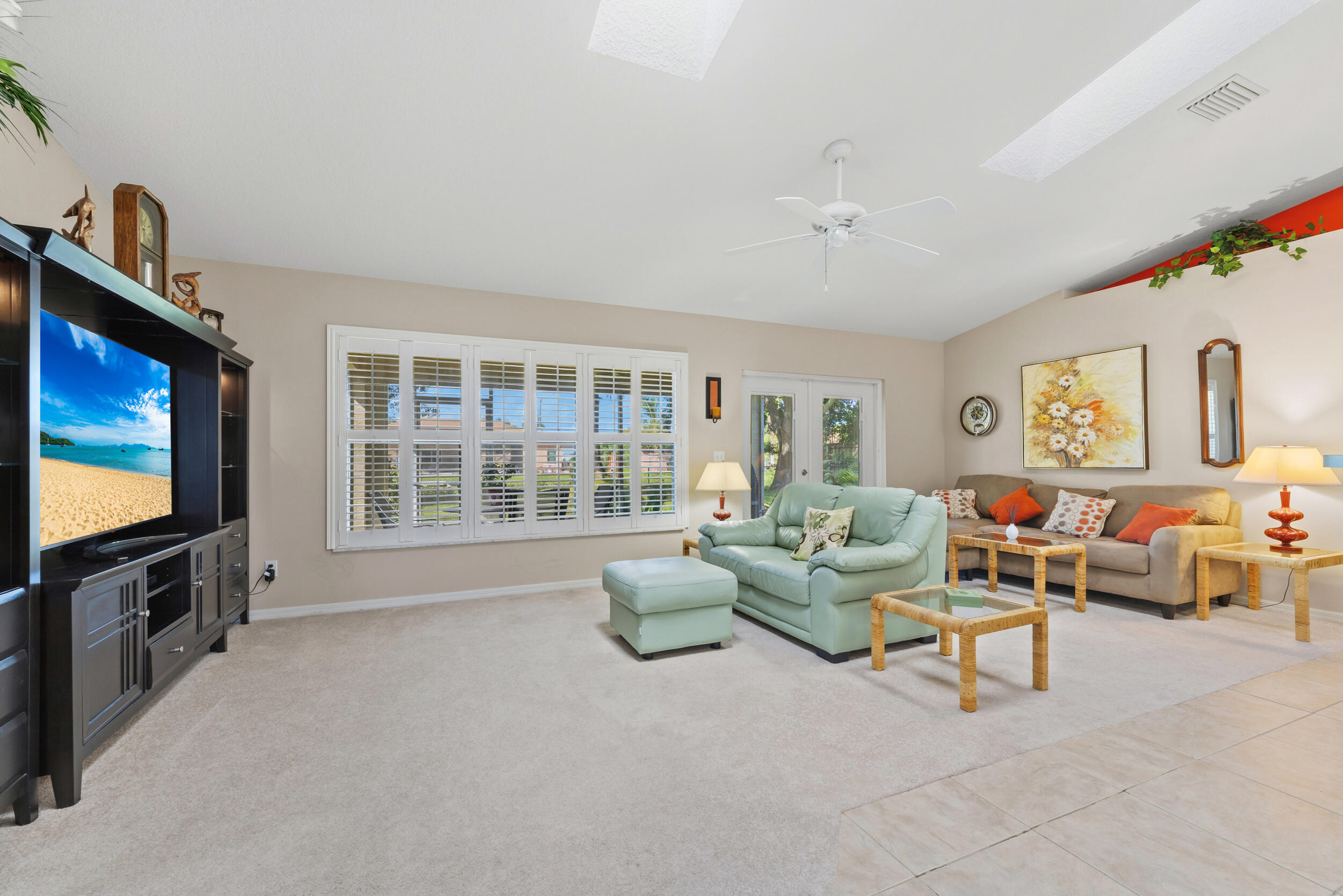 Living area featuring a vaulted ceiling with skylights, white plantation shutters, and a ceiling fan