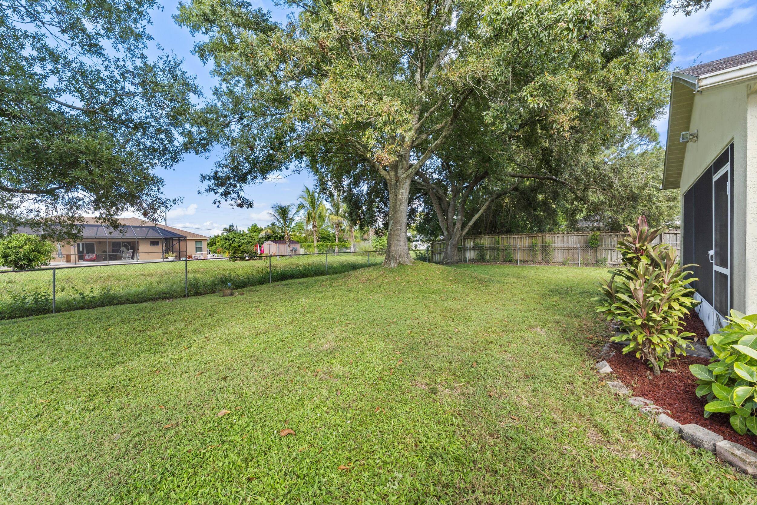 Expansive backyard featuring a fenced perimeter, mature canopy trees, a grass lawn, and a stone-bordered garden bed
