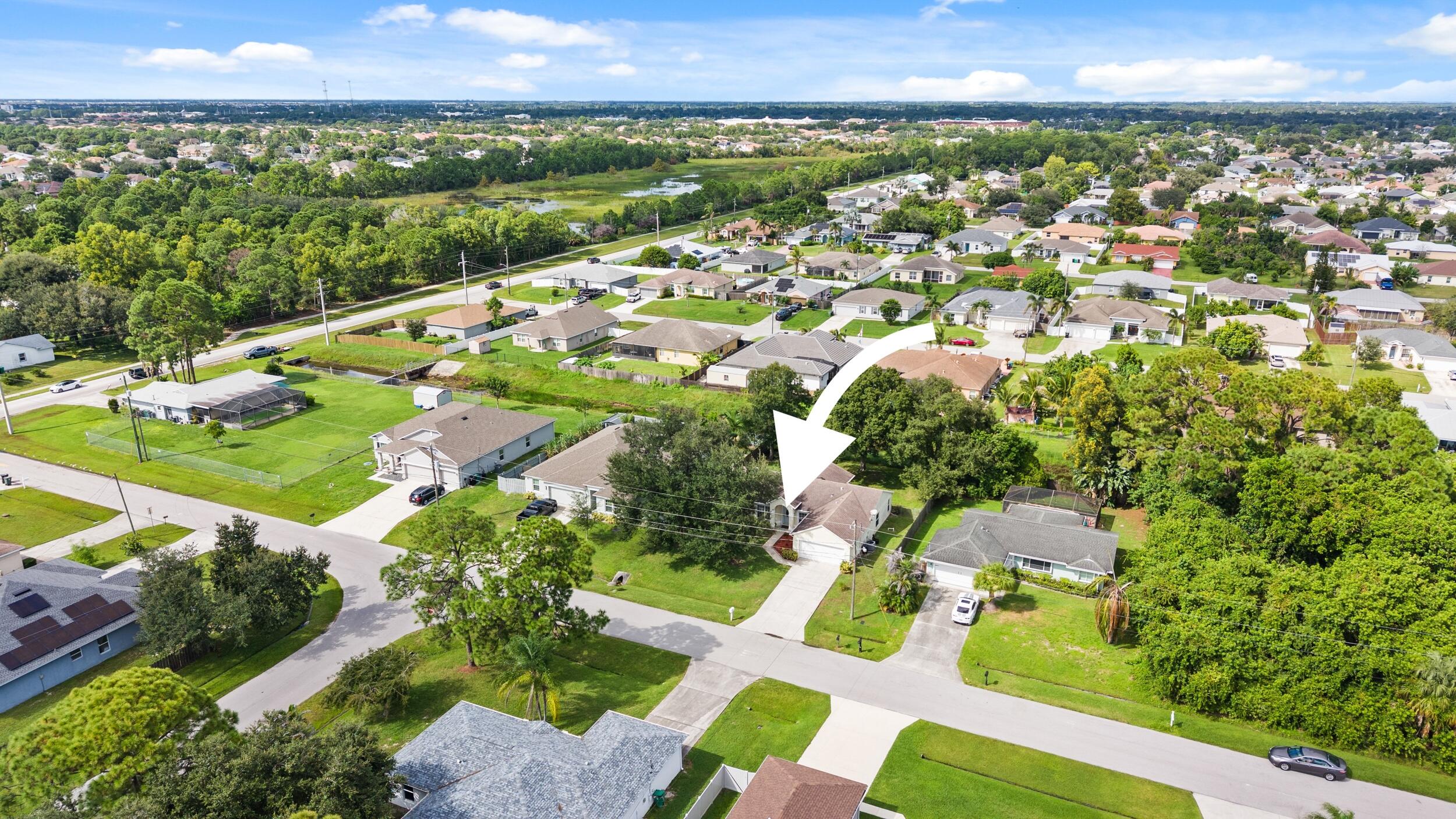 Aerial perspective of a single-story residence featuring a concrete driveway, multi-gabled roofline, and established landscaping