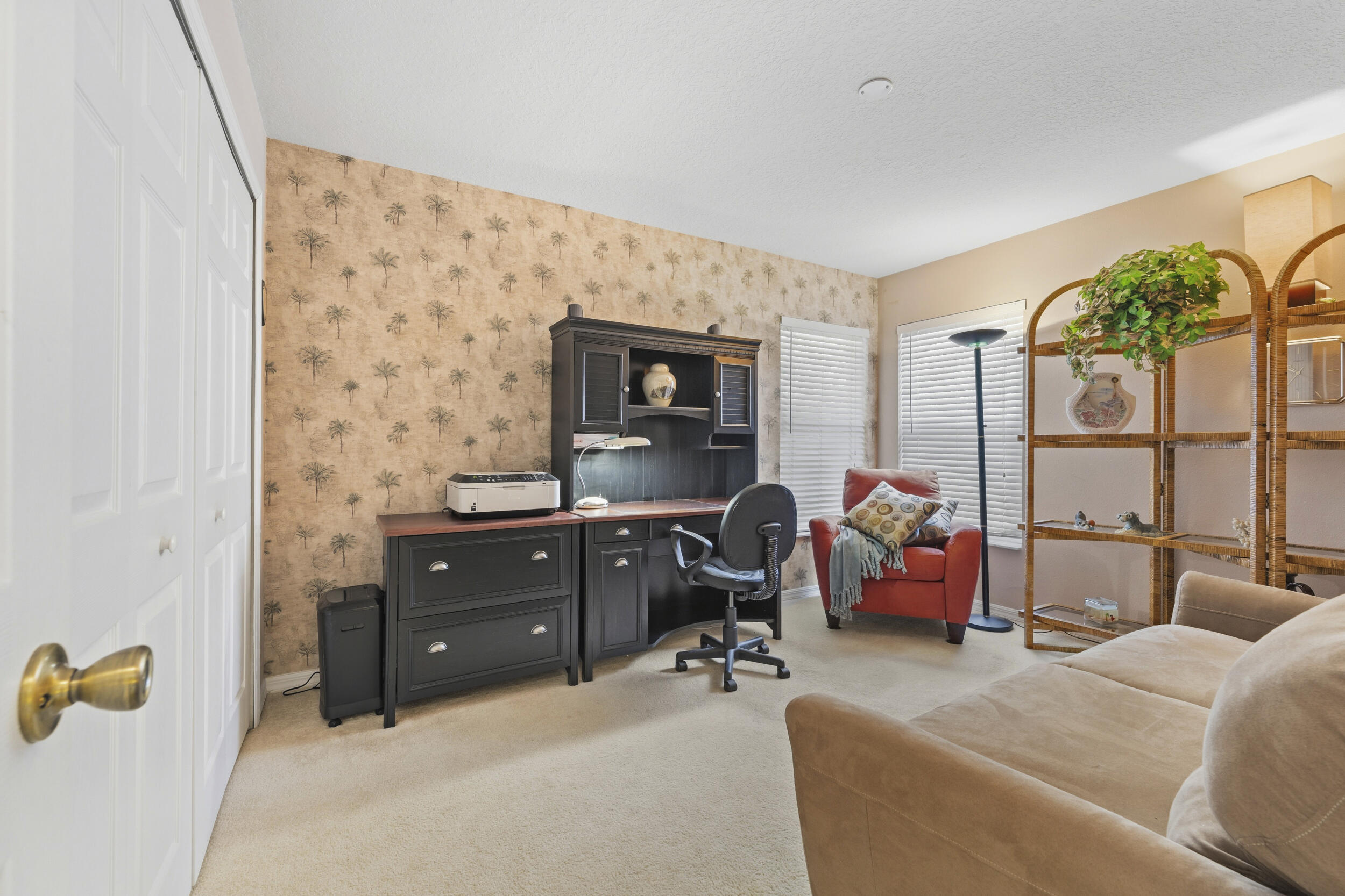 Room featuring neutral wall-to-wall carpeting, dual-door closet with polished brass hardware, and accent wallpaper