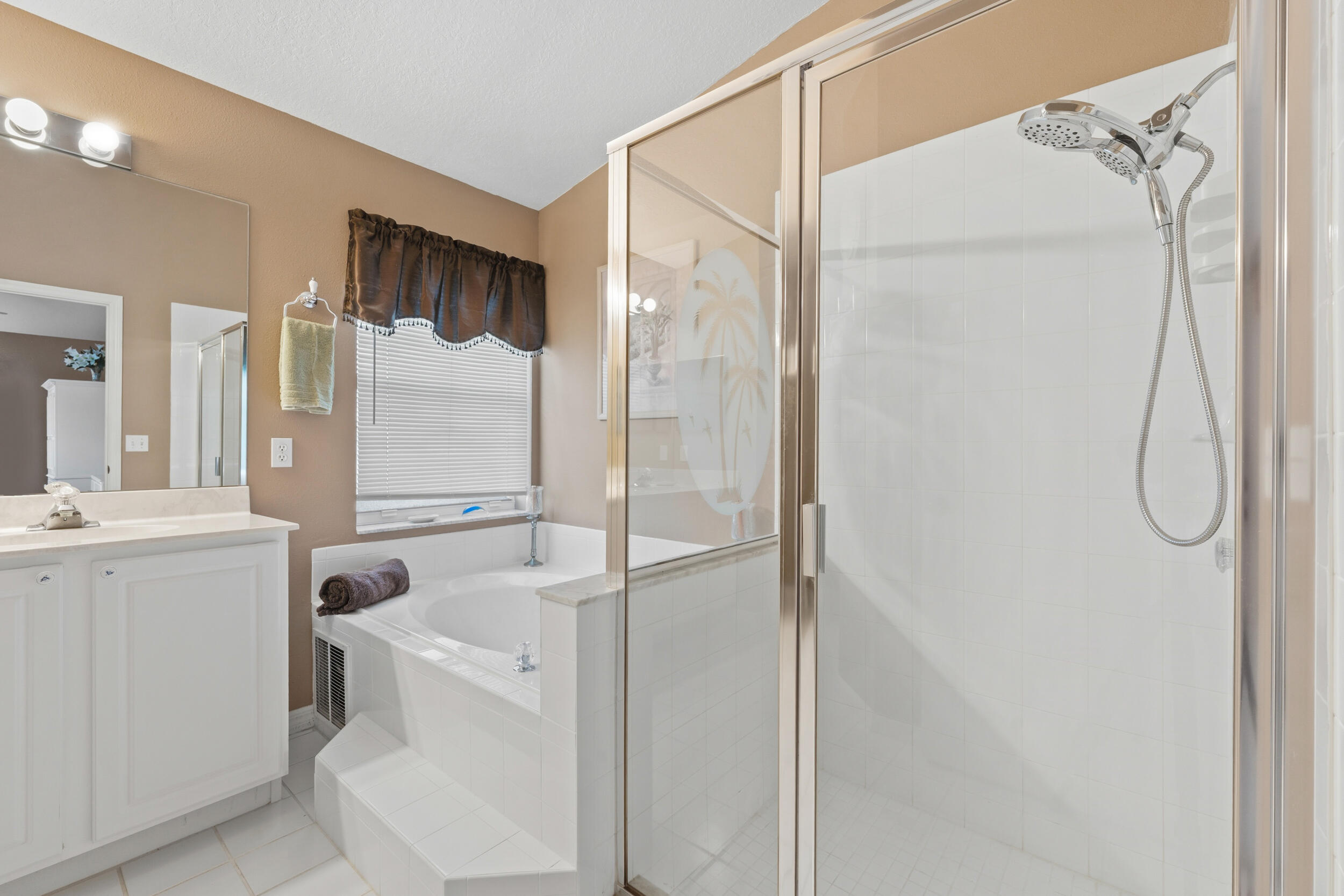 Bathroom featuring a walk-in shower with a glass enclosure, a white soaking tub set in a tile surround, a vanity with white cabinetry, and wall-mounted light fixtures