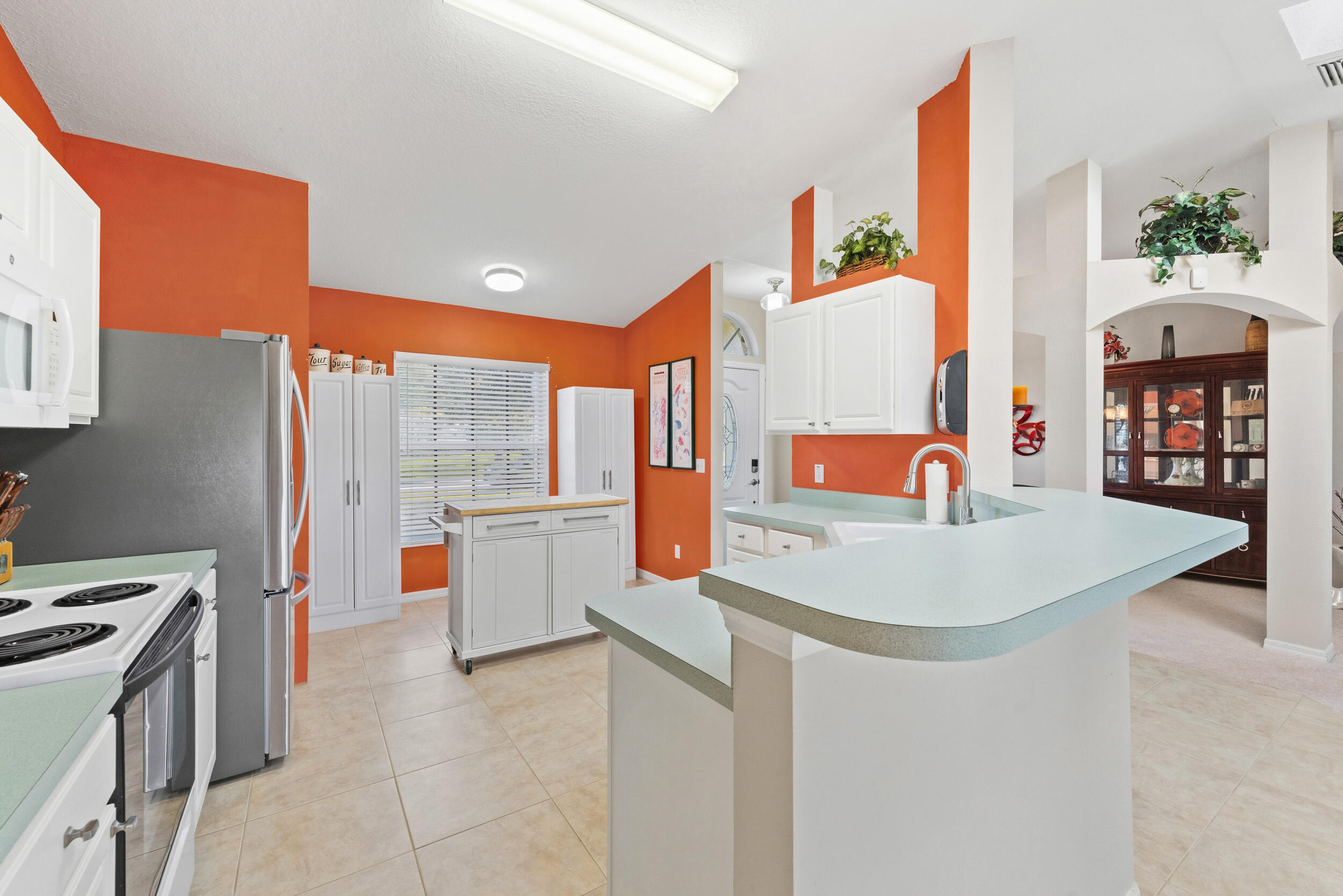 Kitchen featuring white shaker-style cabinetry, breakfast bar, solid-surface countertops, tile flooring, and vaulted ceiling