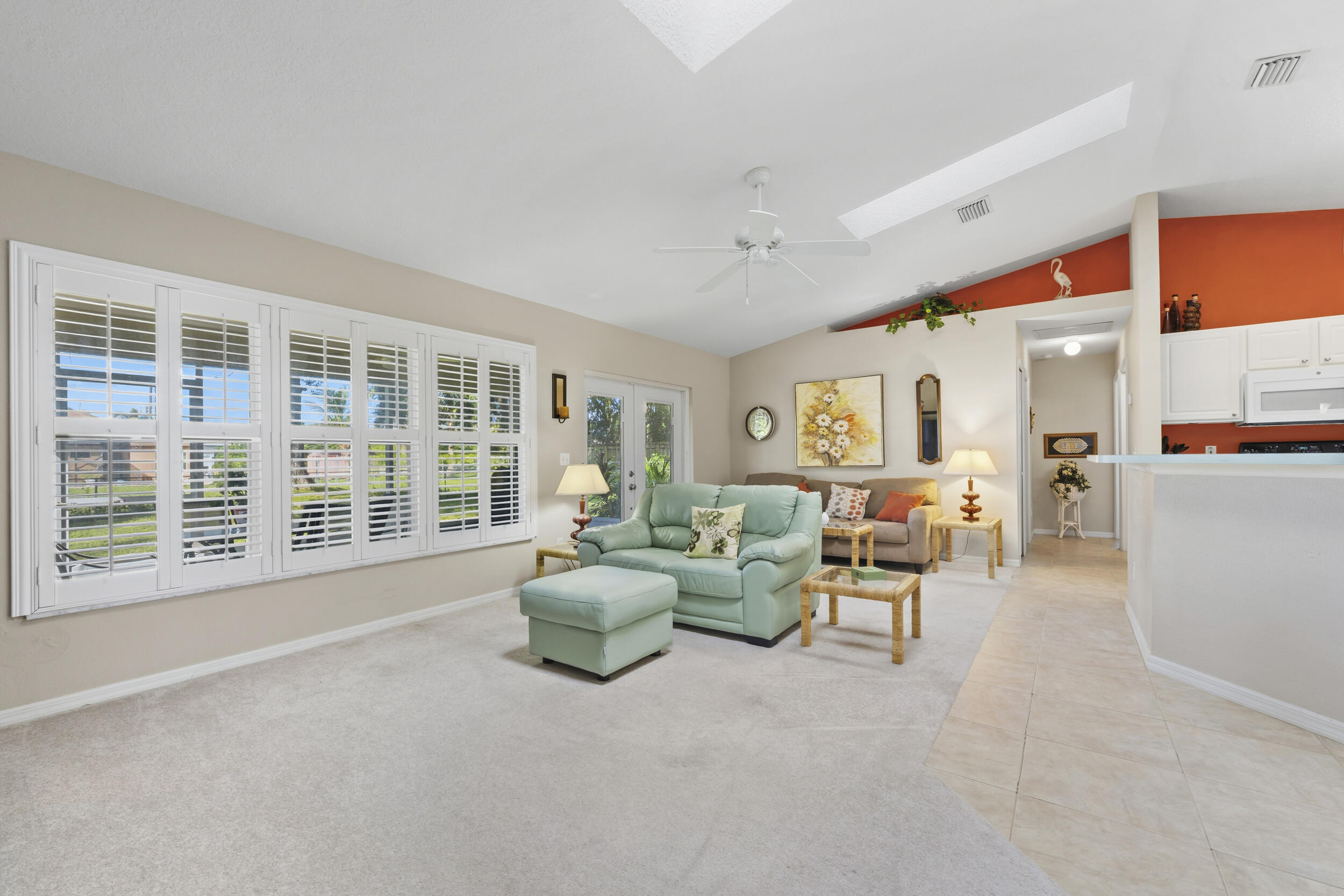 Vaulted ceilings with integrated skylights, plantation shutters, ceiling fan, and ceramic tile flooring