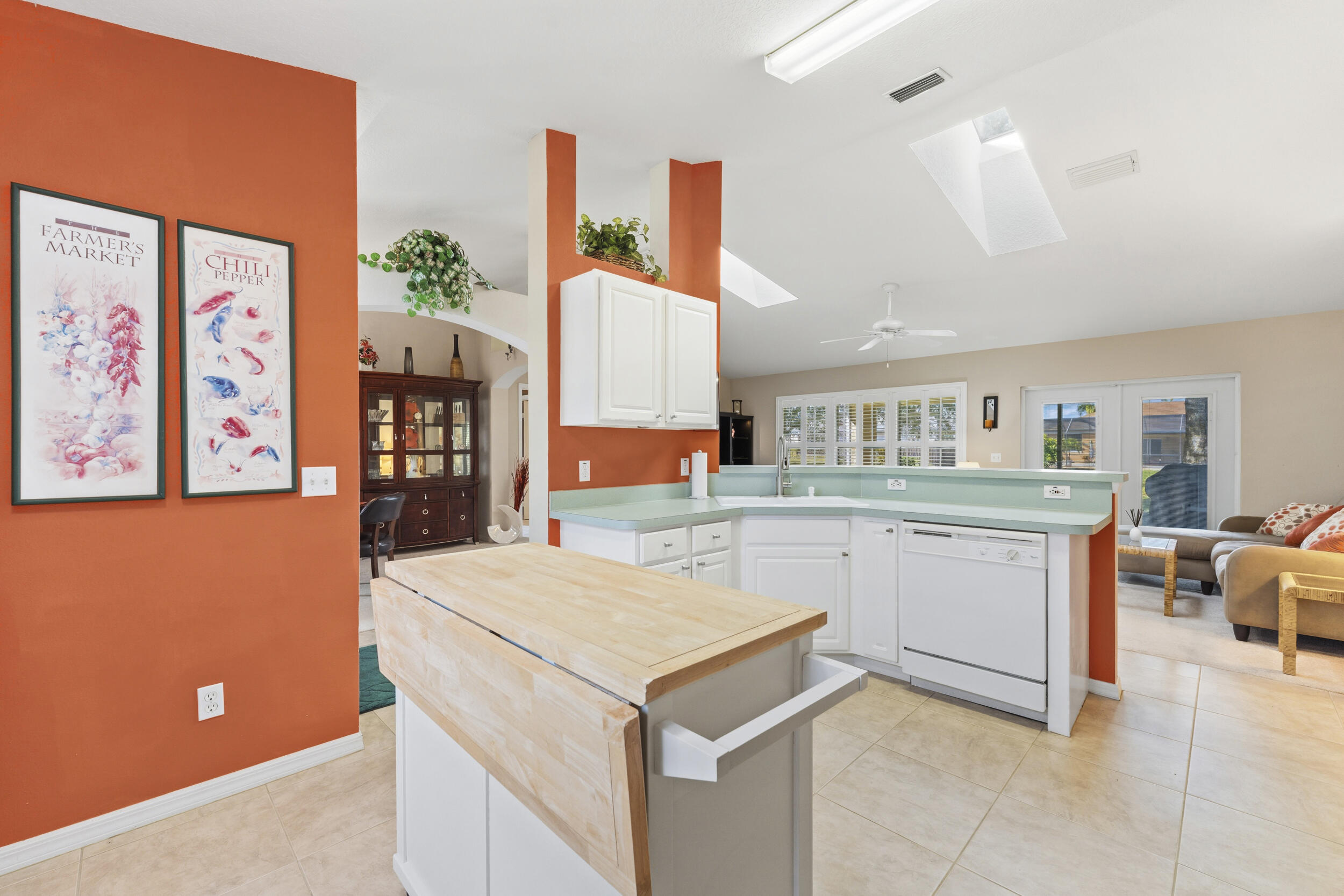 Kitchen featuring a portable wood-top island, white cabinetry, solid-surface countertops, tile flooring, and vaulted ceilings with skylights
