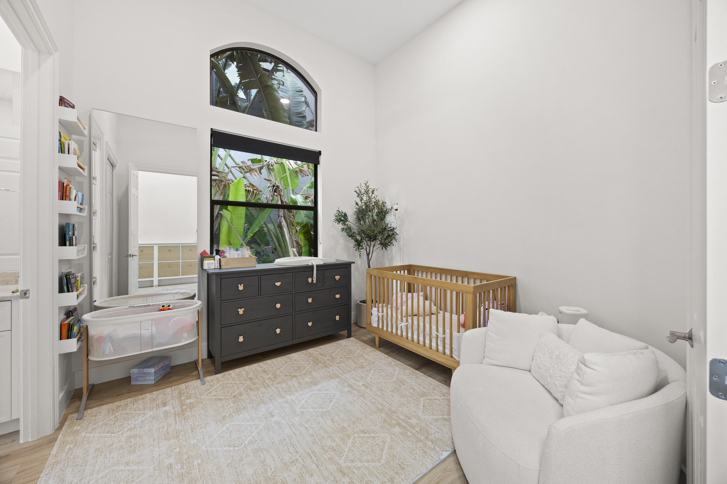 High ceilings featuring a prominent arched window and light-toned wood-finish flooring