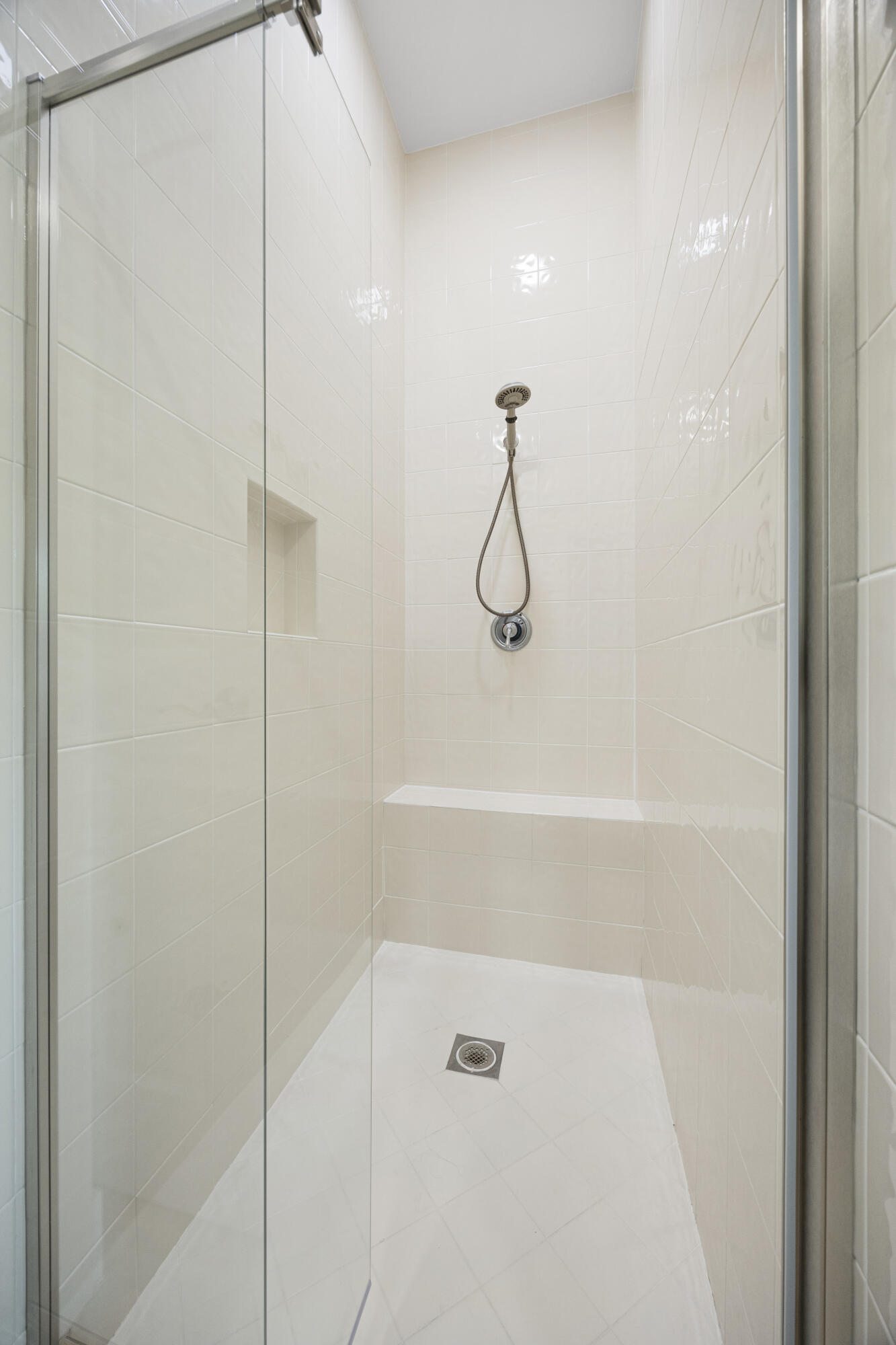 Walk-in shower featuring floor-to-ceiling tile, a frameless glass door, a built-in bench, an integrated wall niche, and a handheld shower fixture