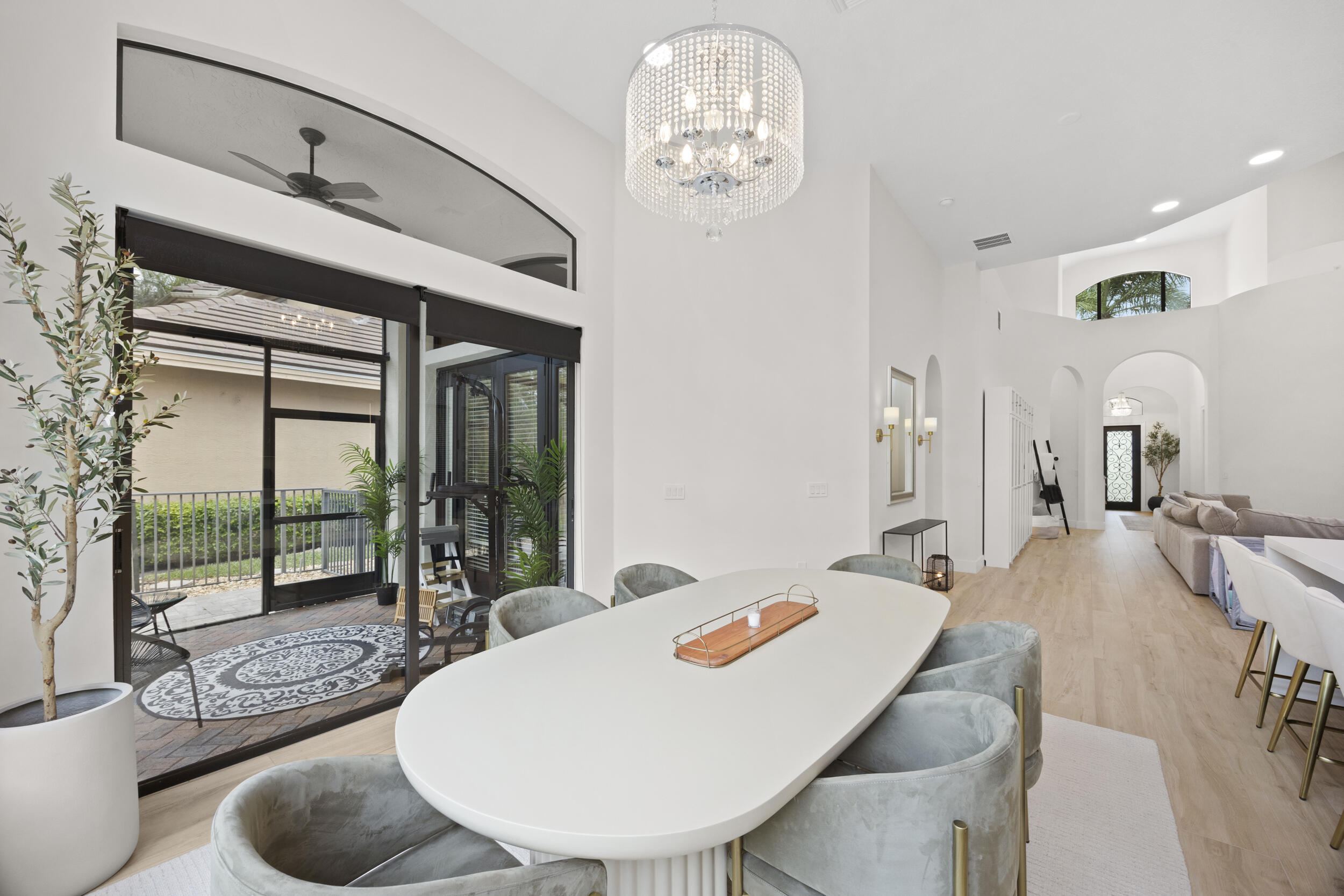 High-ceilinged interior featuring a tiered crystal chandelier, wood-finish flooring, arched architectural details, and a multi-panel glass sliding door system