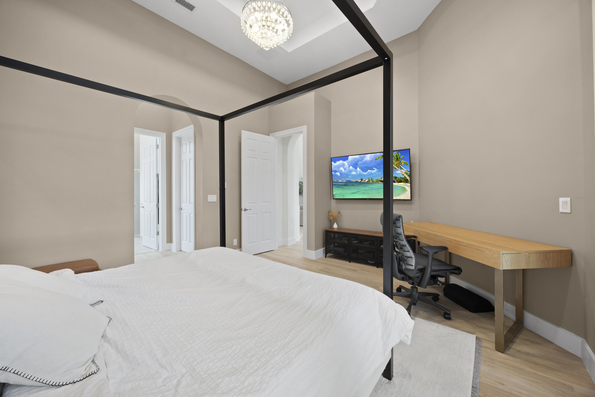 Room featuring high ceilings with a tray ceiling detail, recessed lighting, a decorative chandelier, archway architectural elements, and light-toned wood-finish flooring