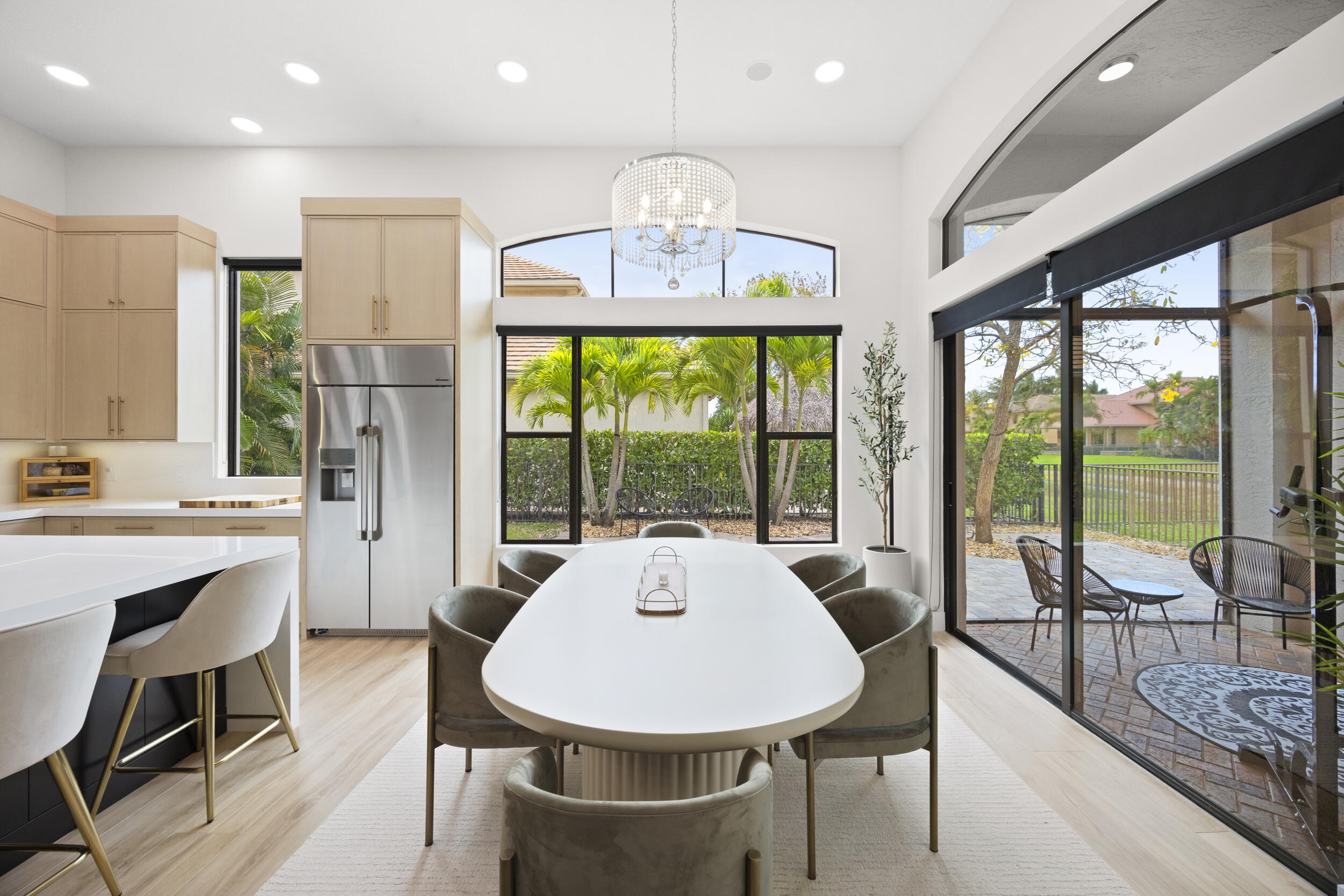 Kitchen and dining area featuring light-tone cabinetry, stainless steel refrigerator, recessed lighting, arched window with a crystal chandelier, and sliding glass doors with access to a paved patio
