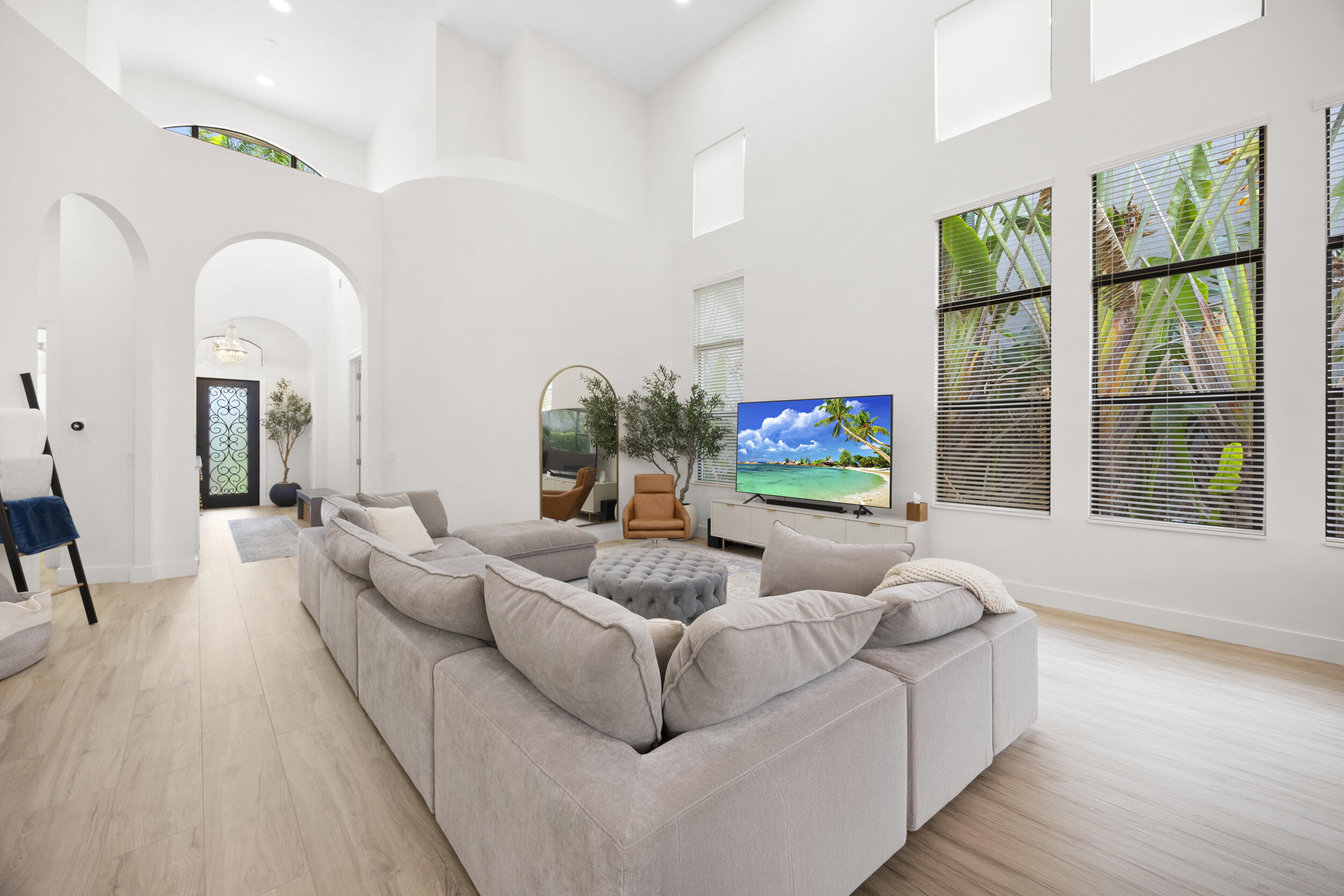 High-ceiling living area featuring arched architectural details, wood-finish flooring, and expansive windows with custom blinds