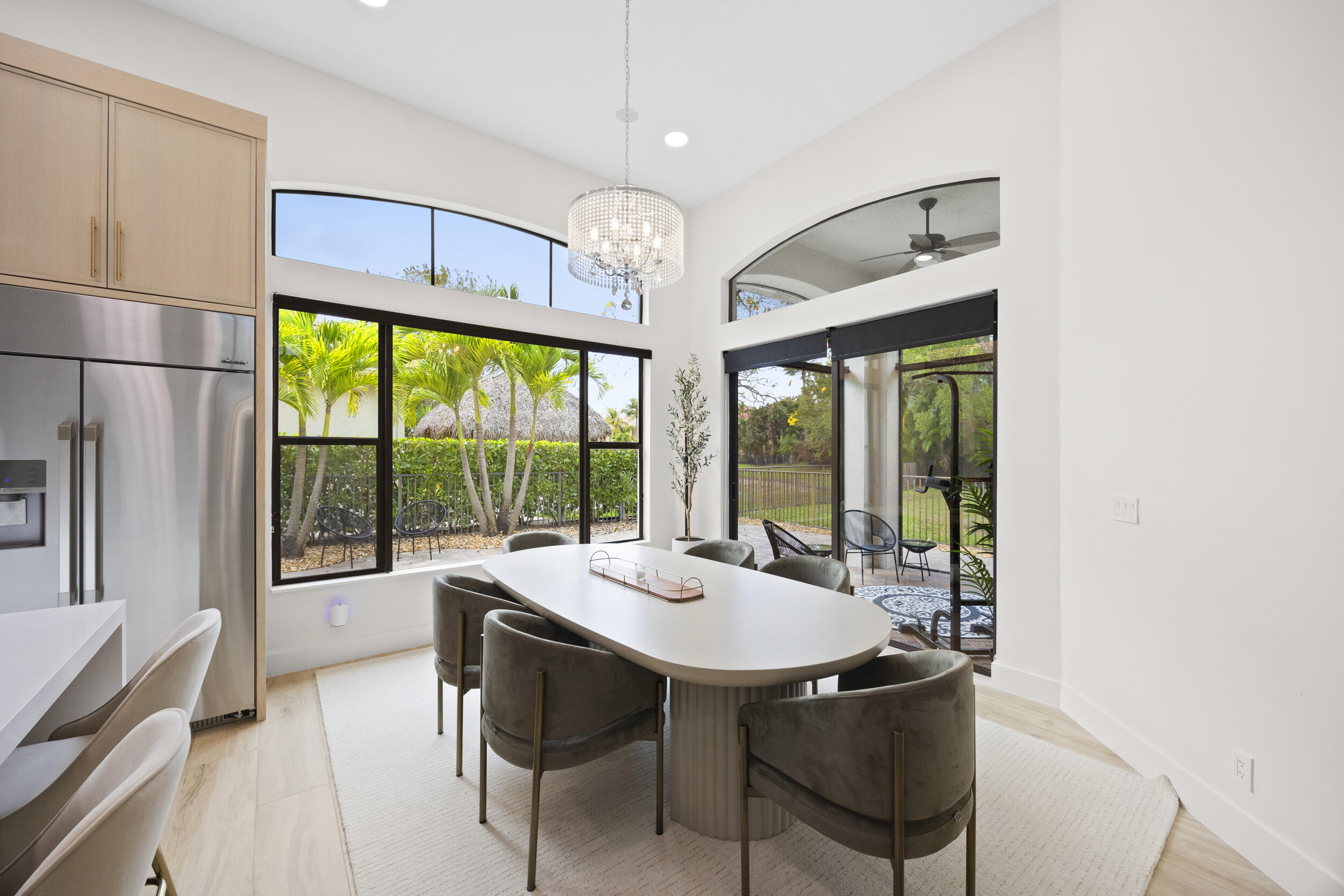Dining area featuring vaulted ceilings, floor-to-ceiling windows with transoms, modern tiered crystal chandelier, and sliding glass doors