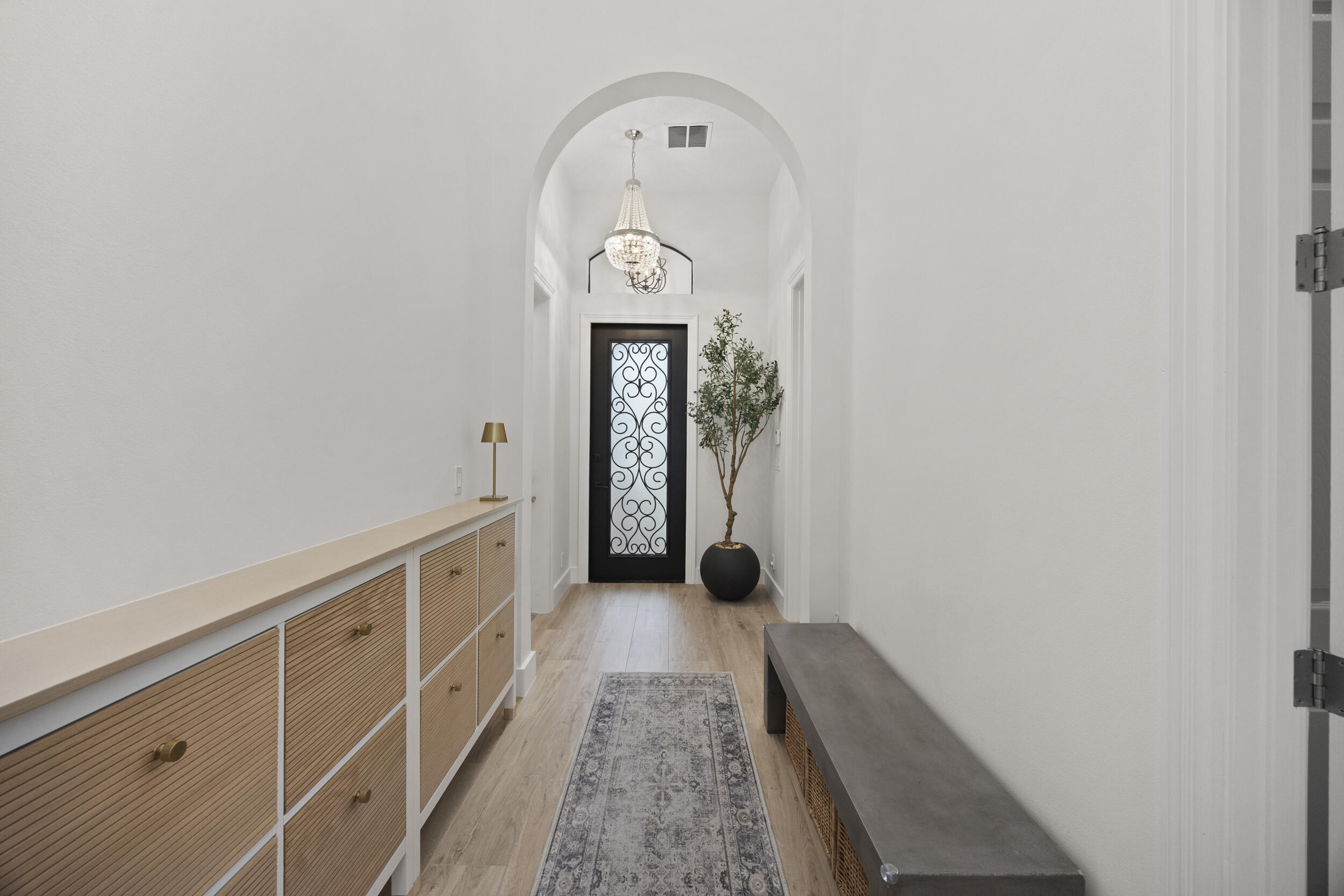 Entryway featuring an arched ceiling, custom built-in cabinetry with textured paneling, wood-finish flooring, and a decorative metal and glass front door accented by an overhead chandelier