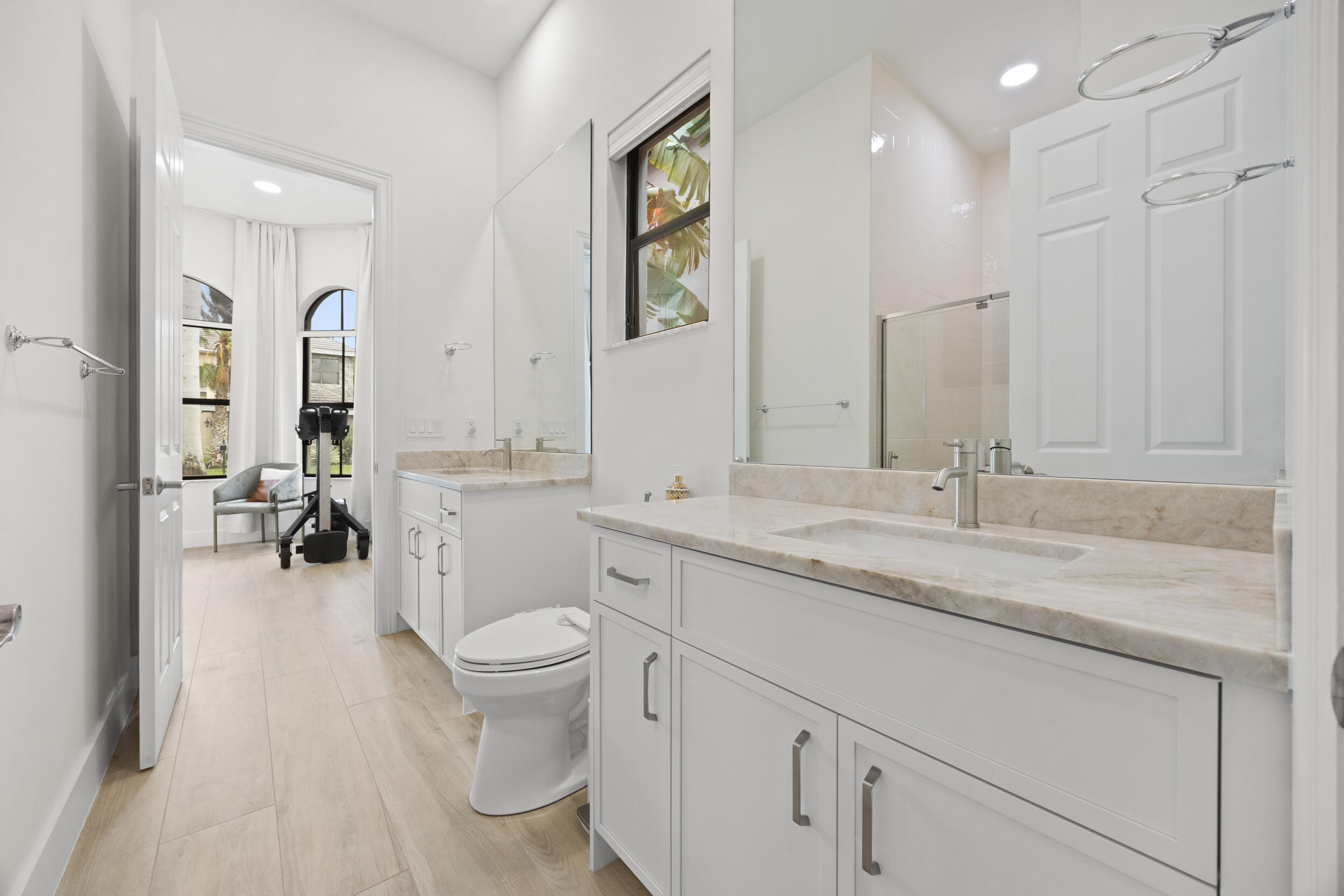Dual-sink vanity with stone countertops and undermount basins, complemented by white cabinetry, full-height wall mirrors, and wood-finish flooring