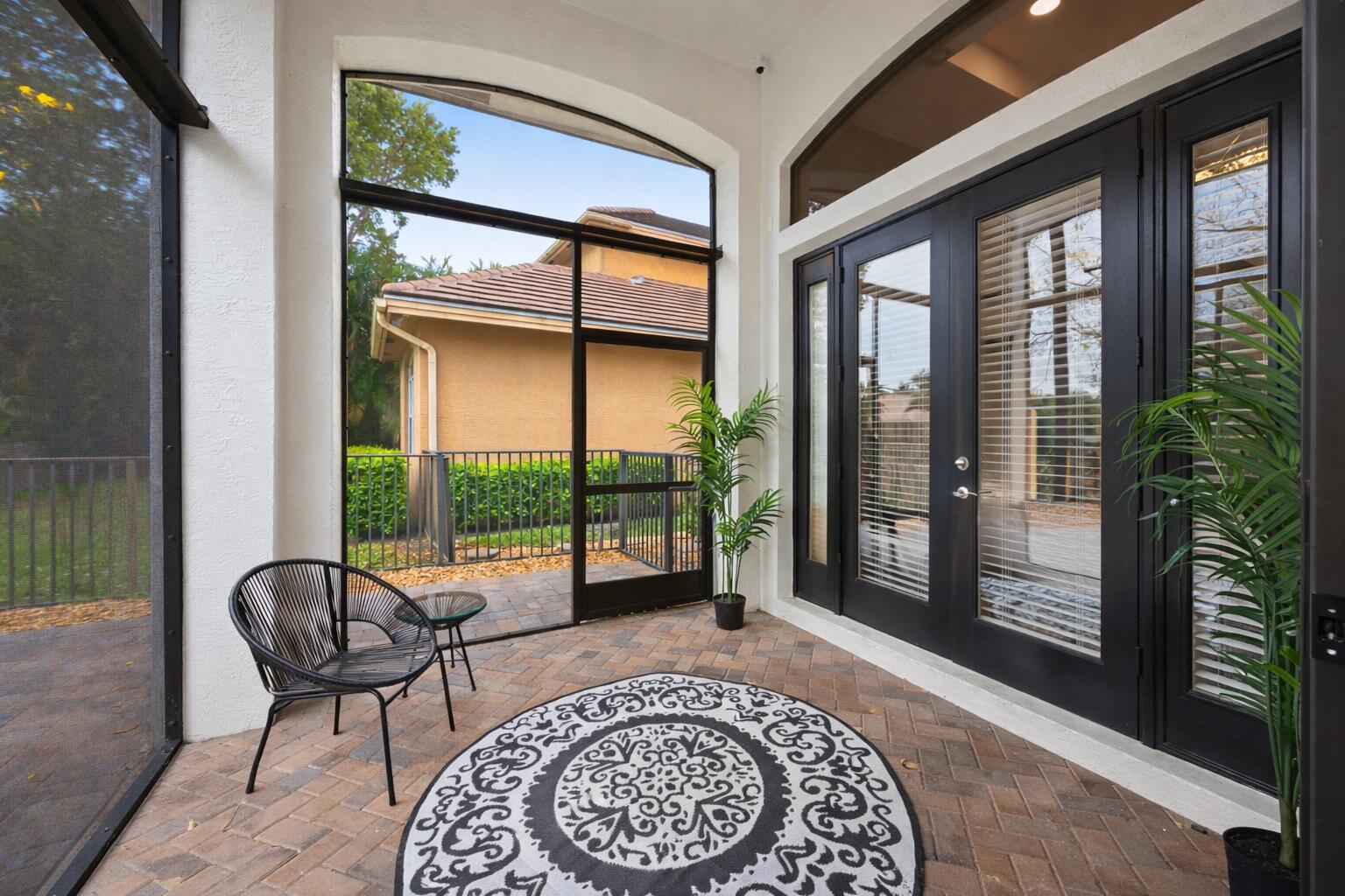 Screened-in patio featuring herringbone-patterned brick flooring, arched floor-to-ceiling windows, and multi-panel black-framed glass doors with transom windows