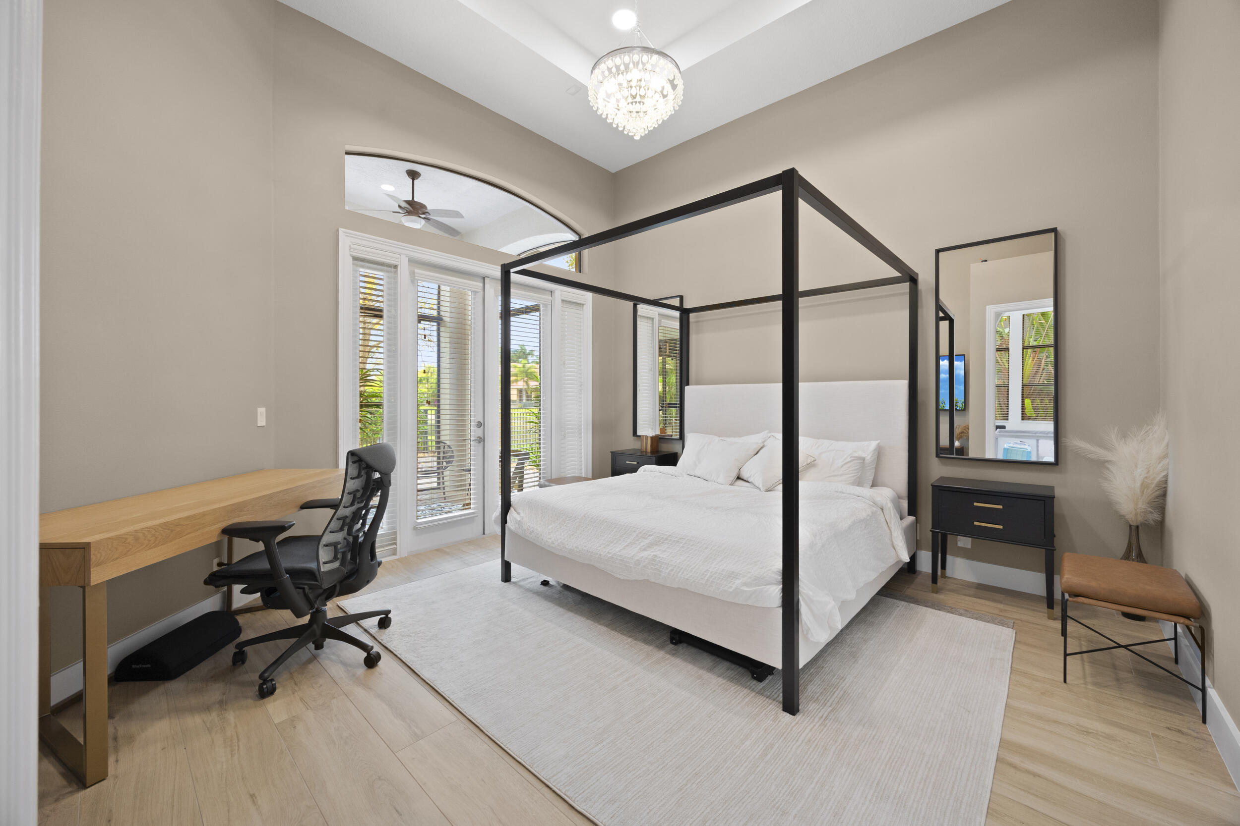 High ceilings with crown molding, tray ceiling detail, wood-finish flooring, glass-paned door with arched transom window, and crystal-style chandelier