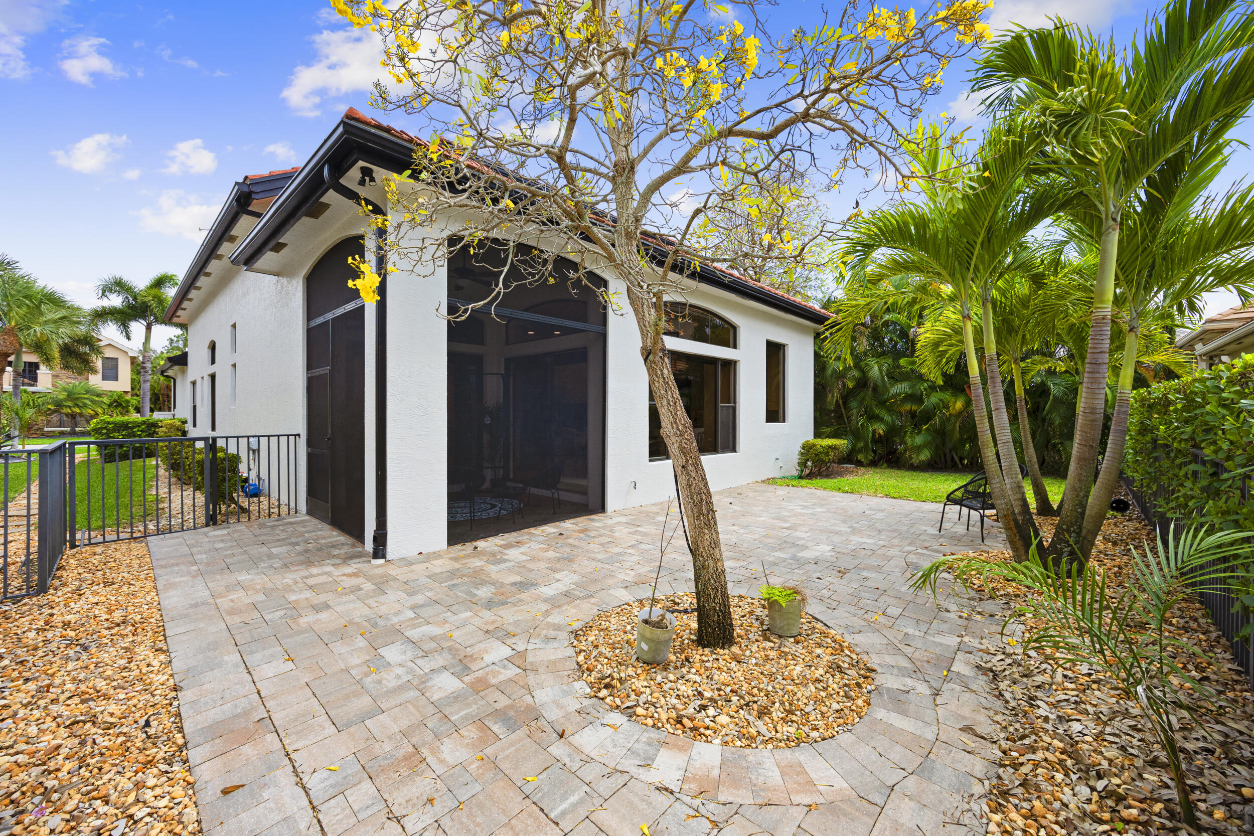 Paved stone patio featuring a screened-in lanai, decorative gravel landscaping, and mature palm trees