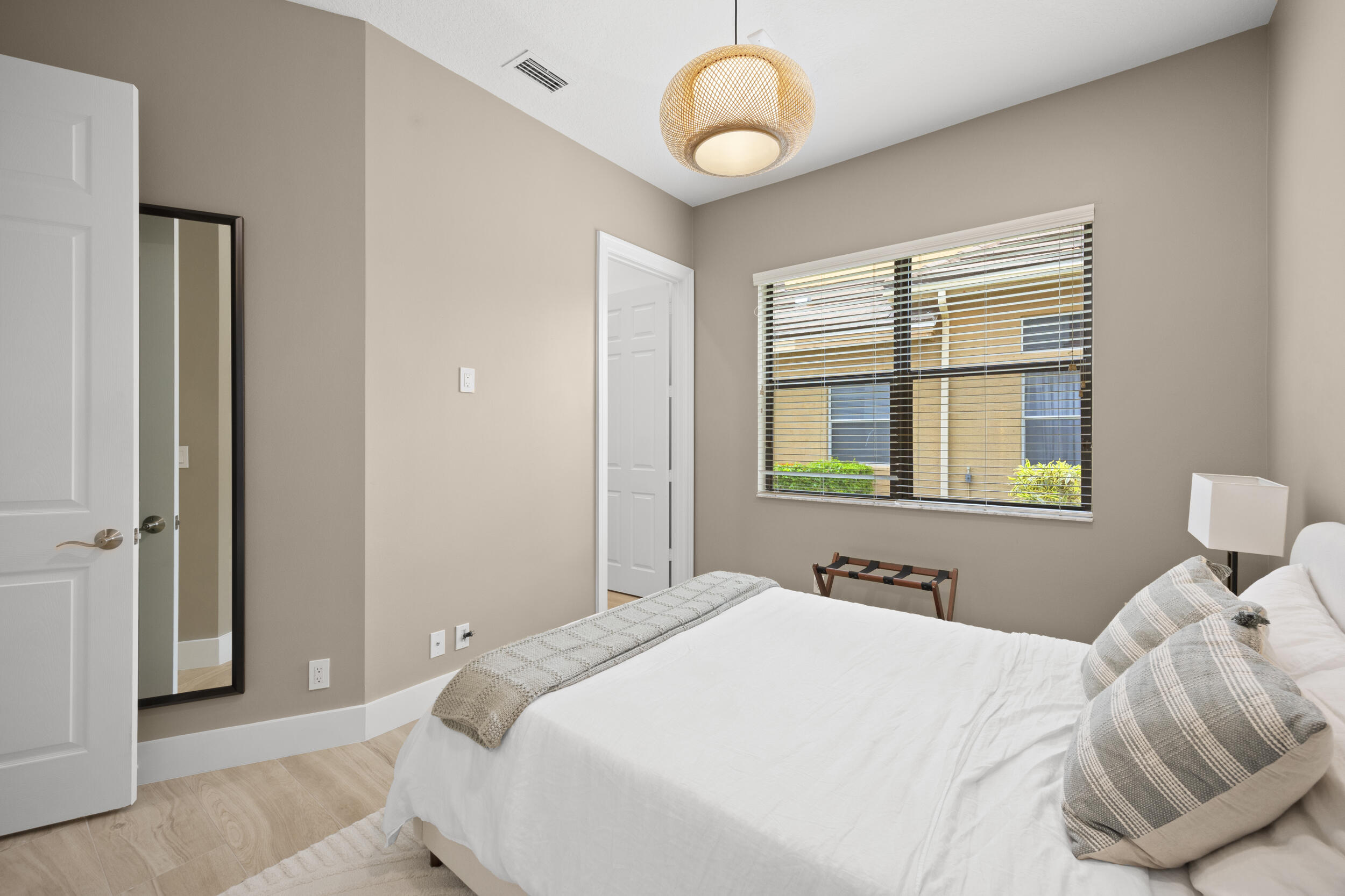 Neutral interior room featuring light wood-finish flooring, a woven pendant light fixture, and a window with integrated blinds