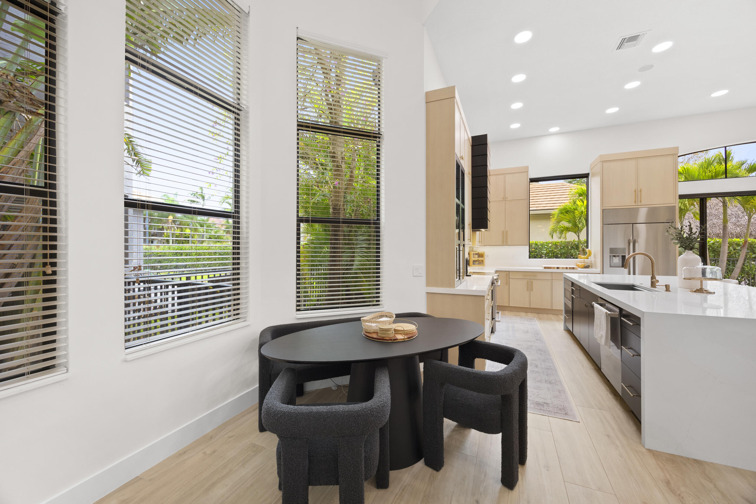 Kitchen featuring light wood-finish cabinetry, a large waterfall-edge island with solid surface countertop, stainless steel refrigerator, recessed lighting, and expansive floor-to-ceiling windows