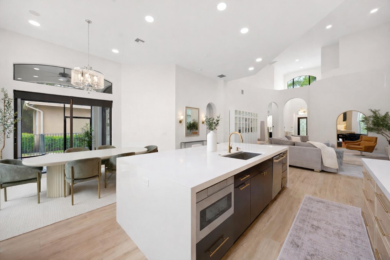 Open-concept kitchen featuring an expansive central island with quartz countertops, custom cabinetry with gold-tone hardware, recessed lighting, and wood-finish flooring