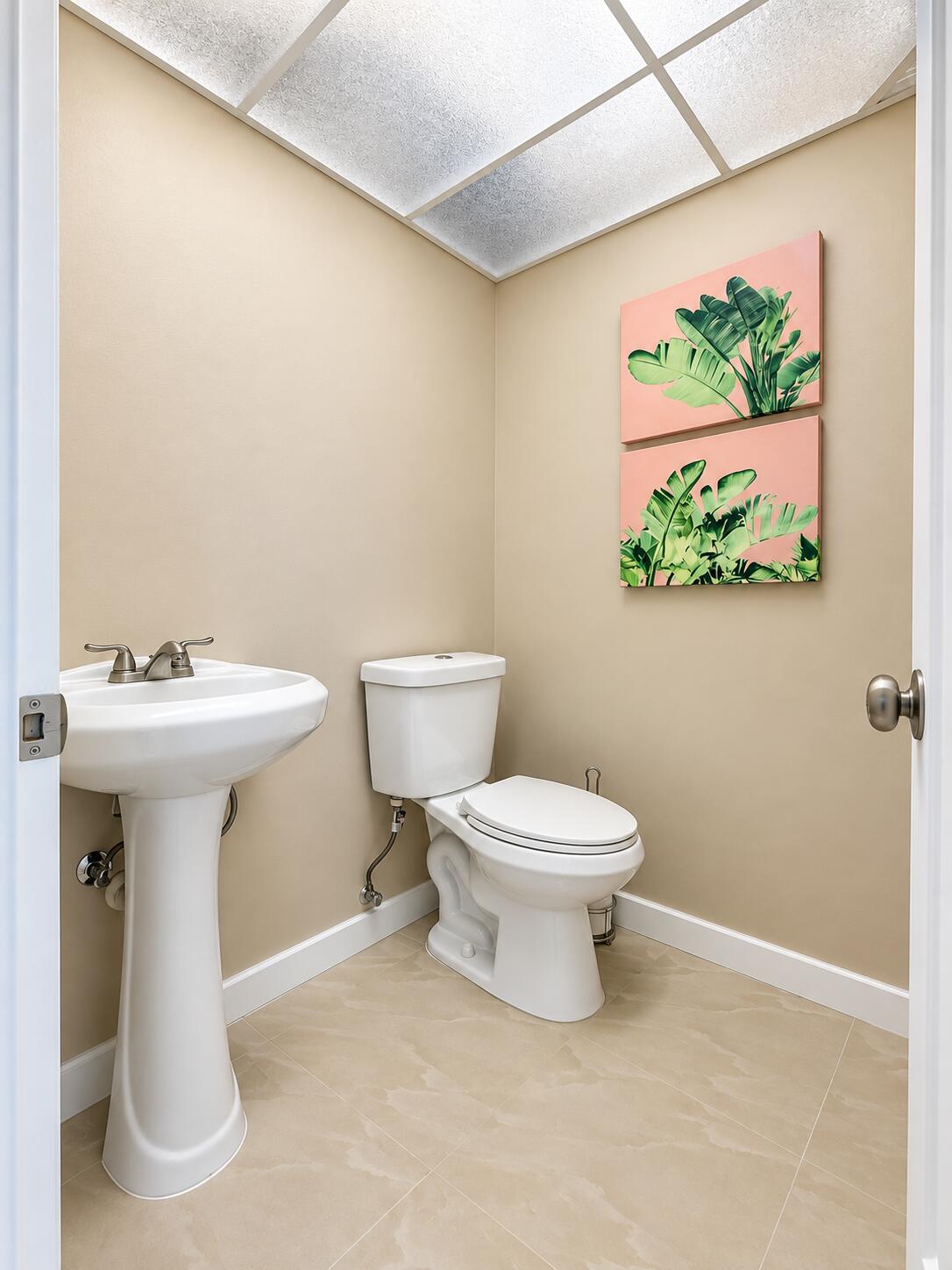 Pedestal sink with two-handle faucet, white ceramic toilet, tile flooring, and drop ceiling with integrated lighting