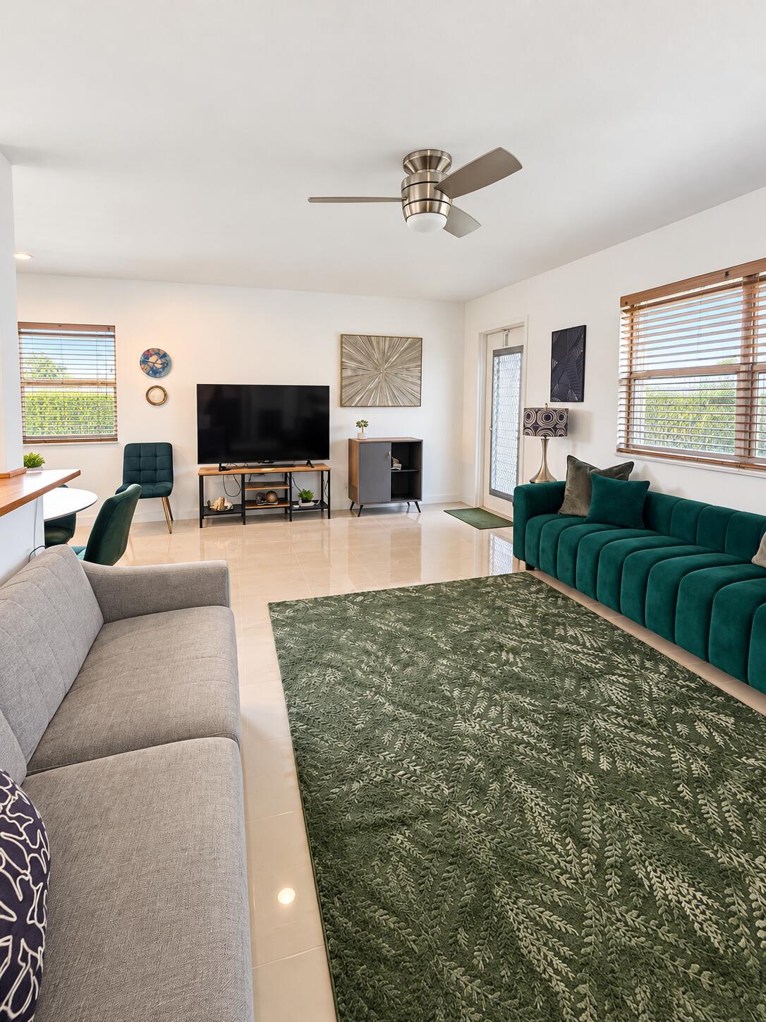 Neutral tile flooring, ceiling fan with light fixture, and multiple windows featuring horizontal blinds