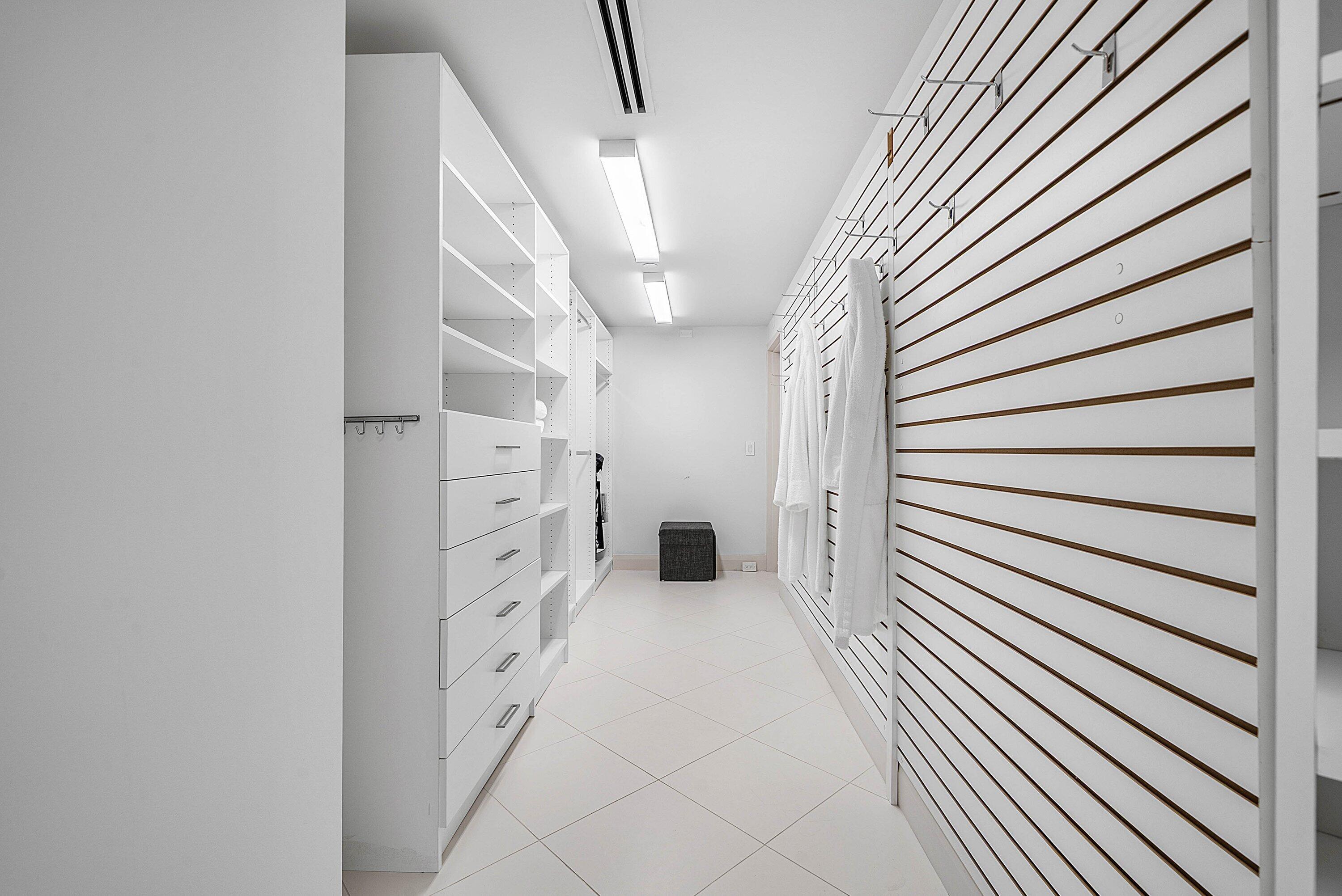 Walk-in closet featuring white built-in cabinetry with integrated drawers, slat-wall organizational system with adjustable hooks, tile flooring, and linear flush-mount lighting
