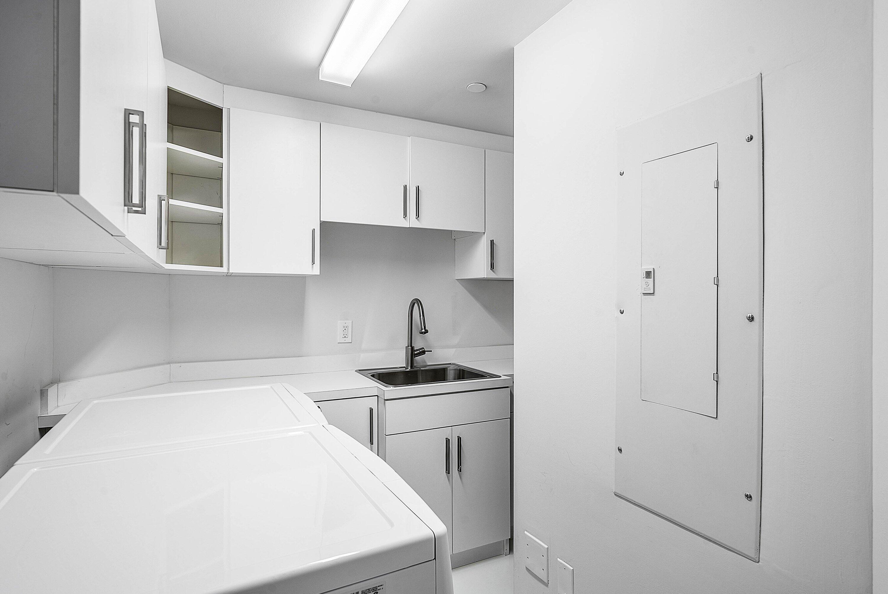 Laundry area featuring white cabinetry, integrated open shelving, a stainless steel sink with a high-arc faucet, and solid-surface countertops