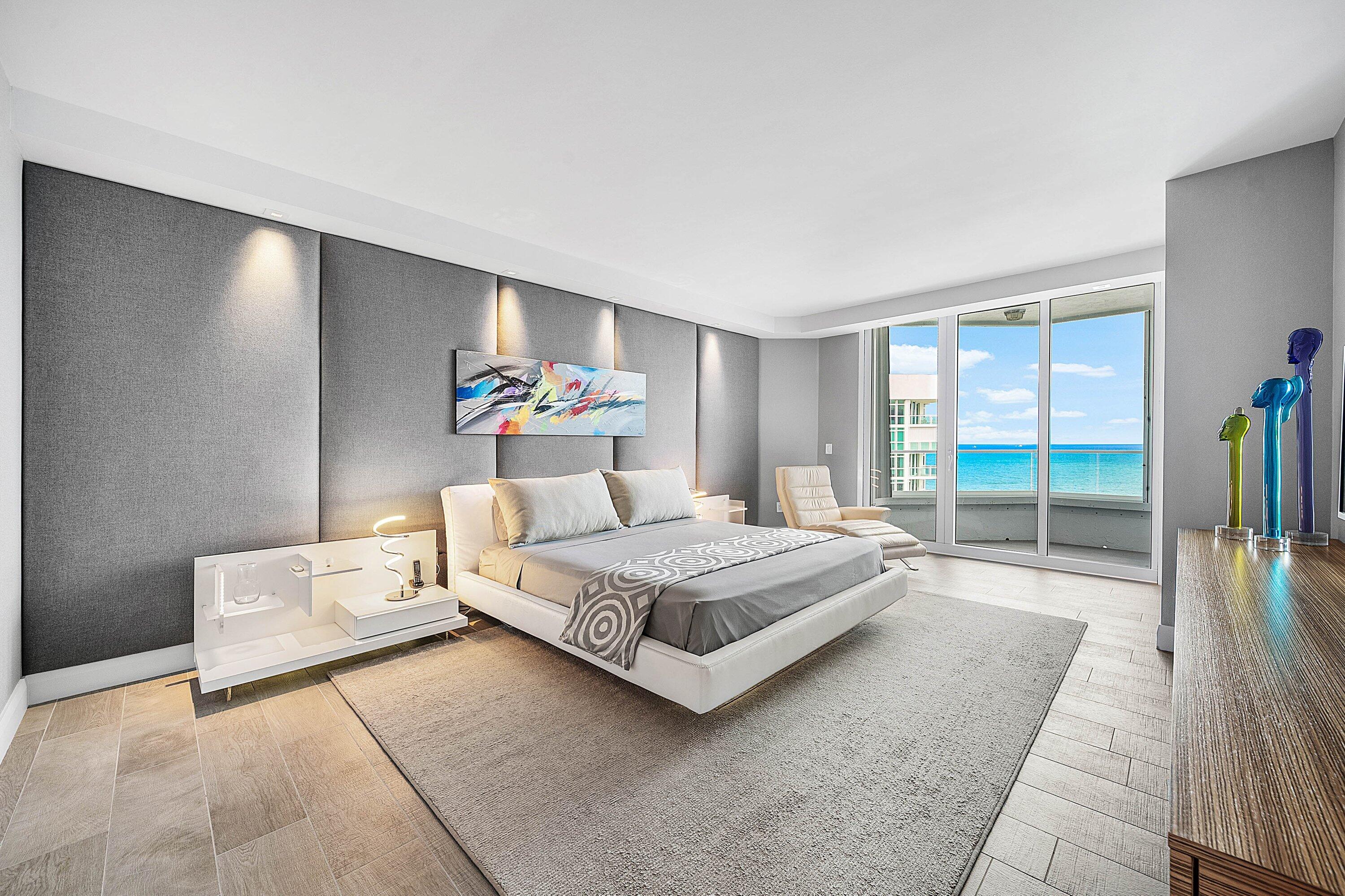 Full-height upholstered wall paneling with integrated accent lighting, tile flooring, and floor-to-ceiling glass sliding doors opening to an ocean backdrop