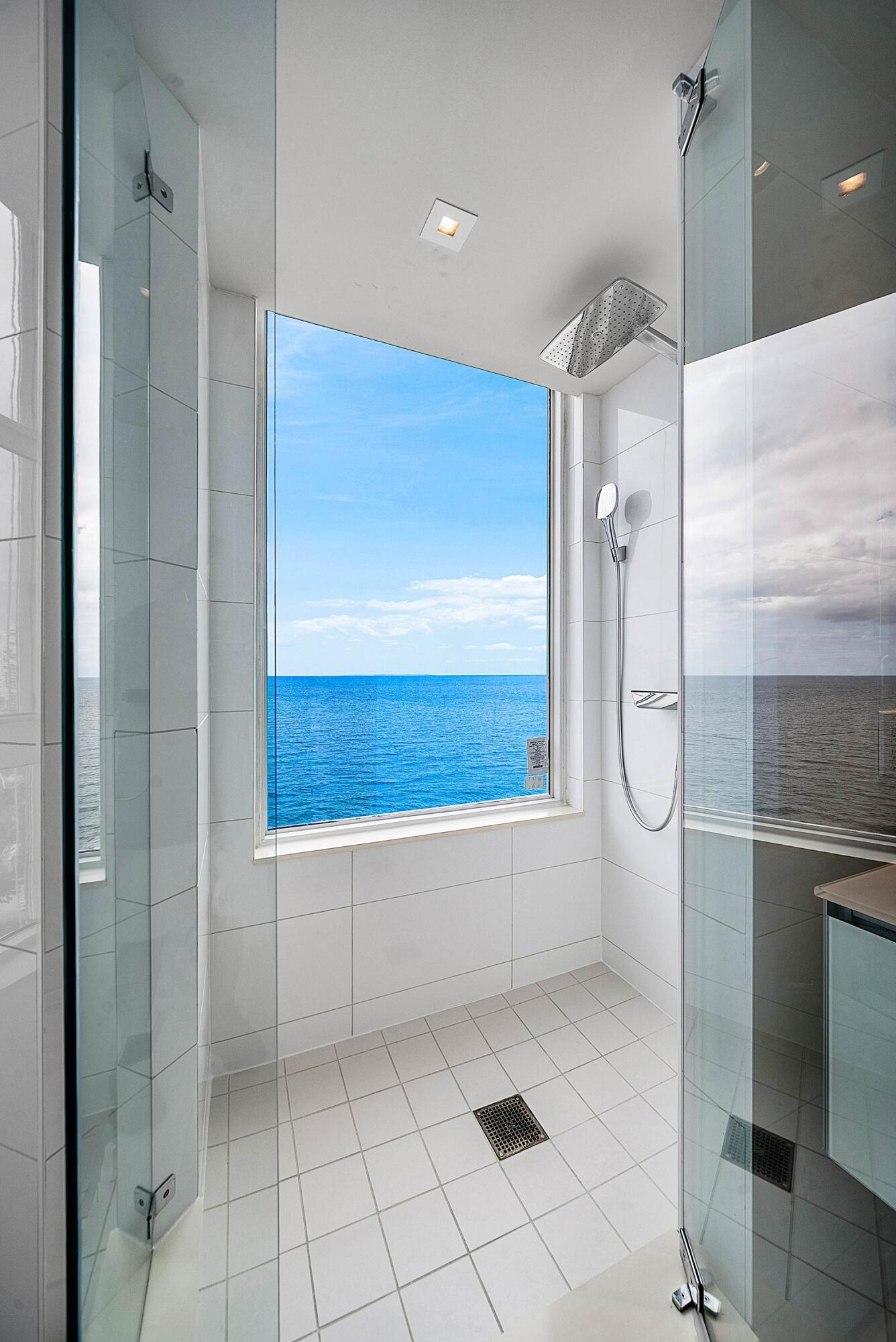 Walk-in shower featuring white tiled walls, a floor-to-ceiling window with water frontage, a rain-style shower head, and a handheld fixture
