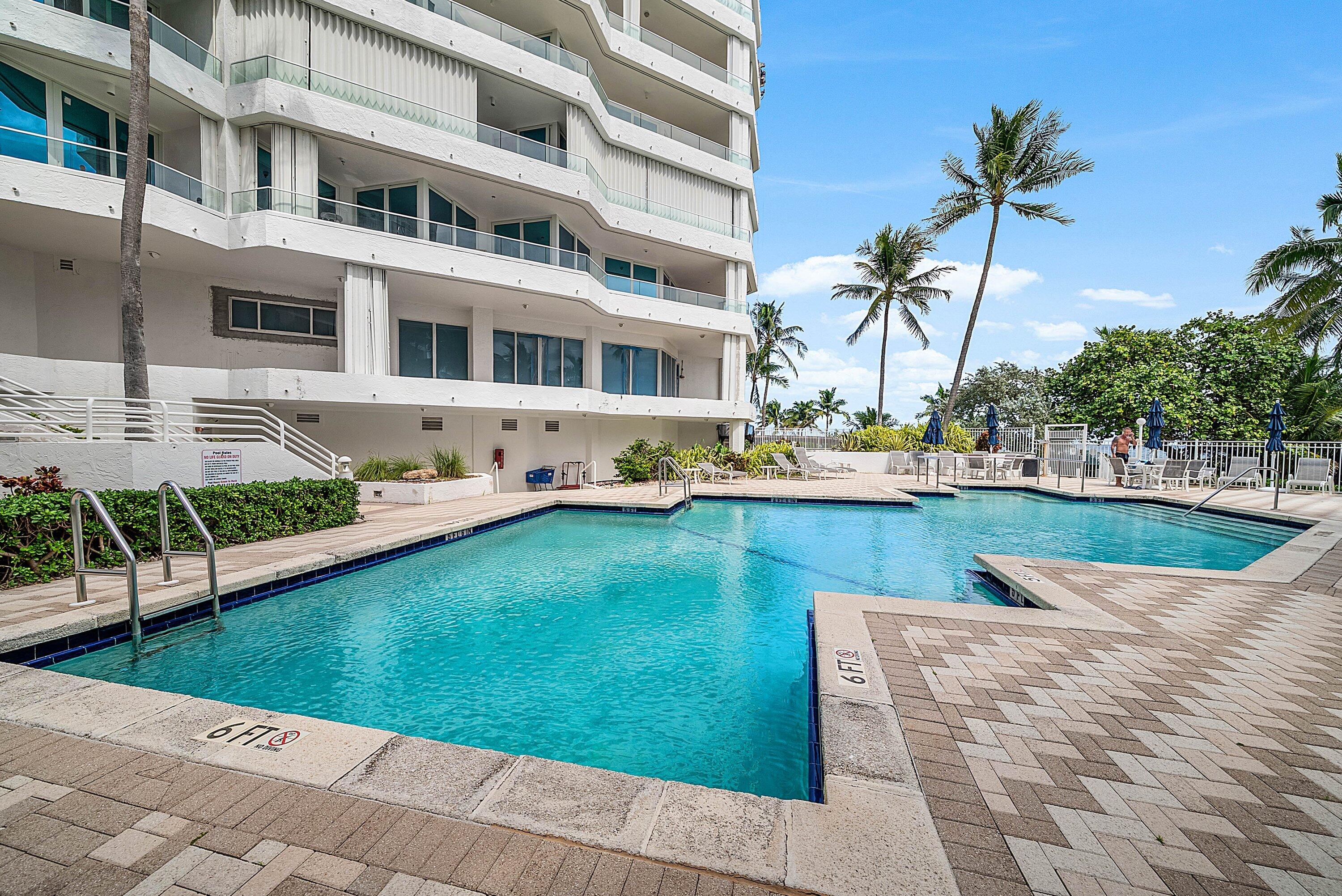 Swimming pool with paver decking, metal handrails, and surrounding mature palm trees