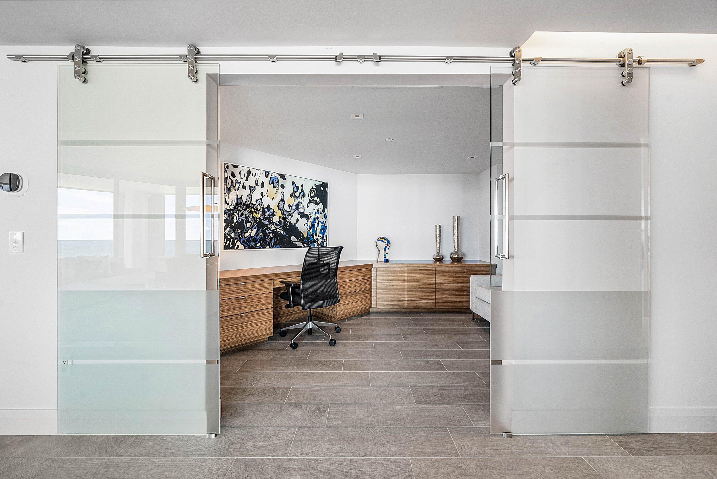 Dual frosted glass sliding doors with stainless steel hardware, wood-finish built-in cabinetry, recessed lighting, and large-format tile flooring