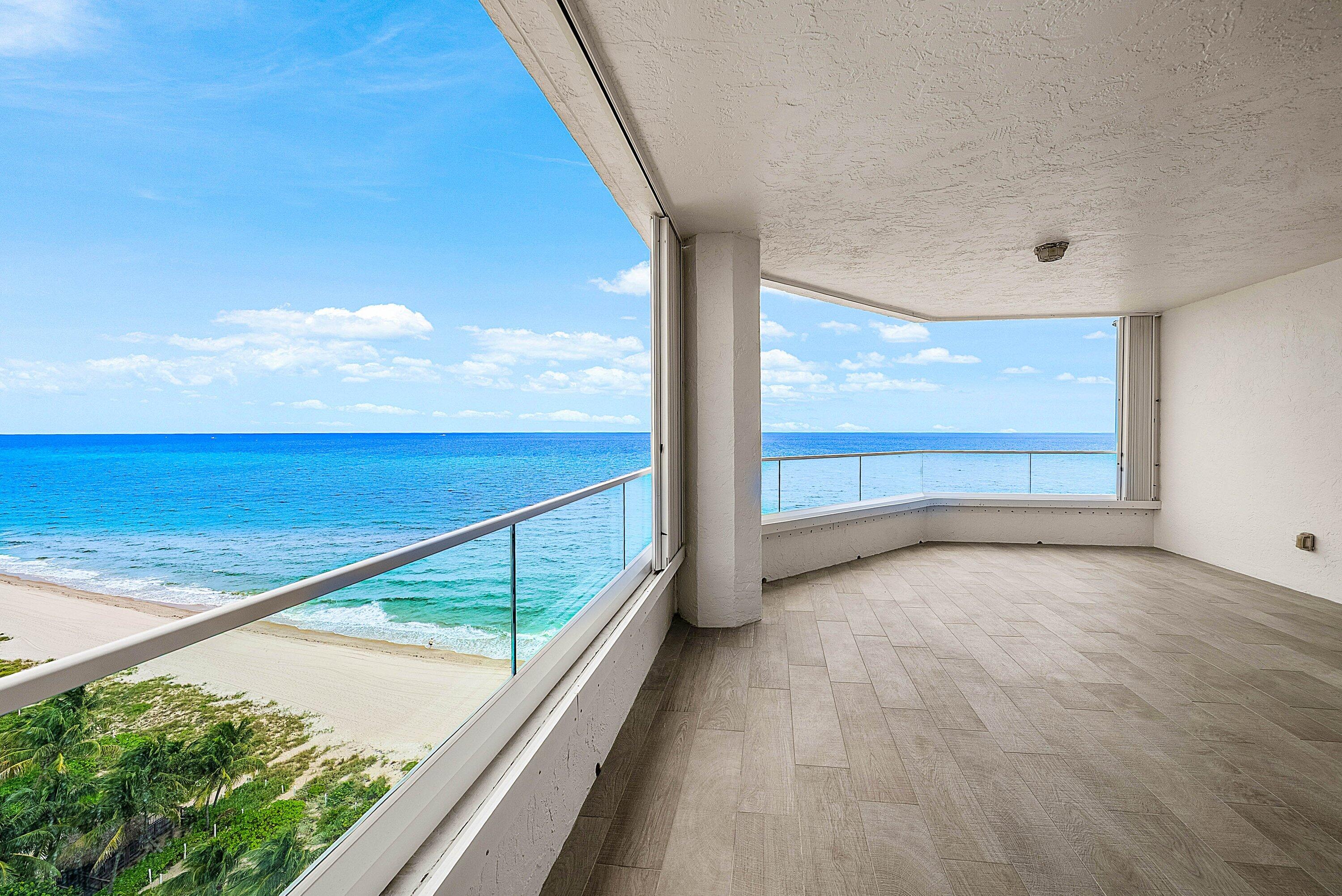 Covered balcony featuring wood-finish tile flooring, glass panel railings, and expansive ocean frontage