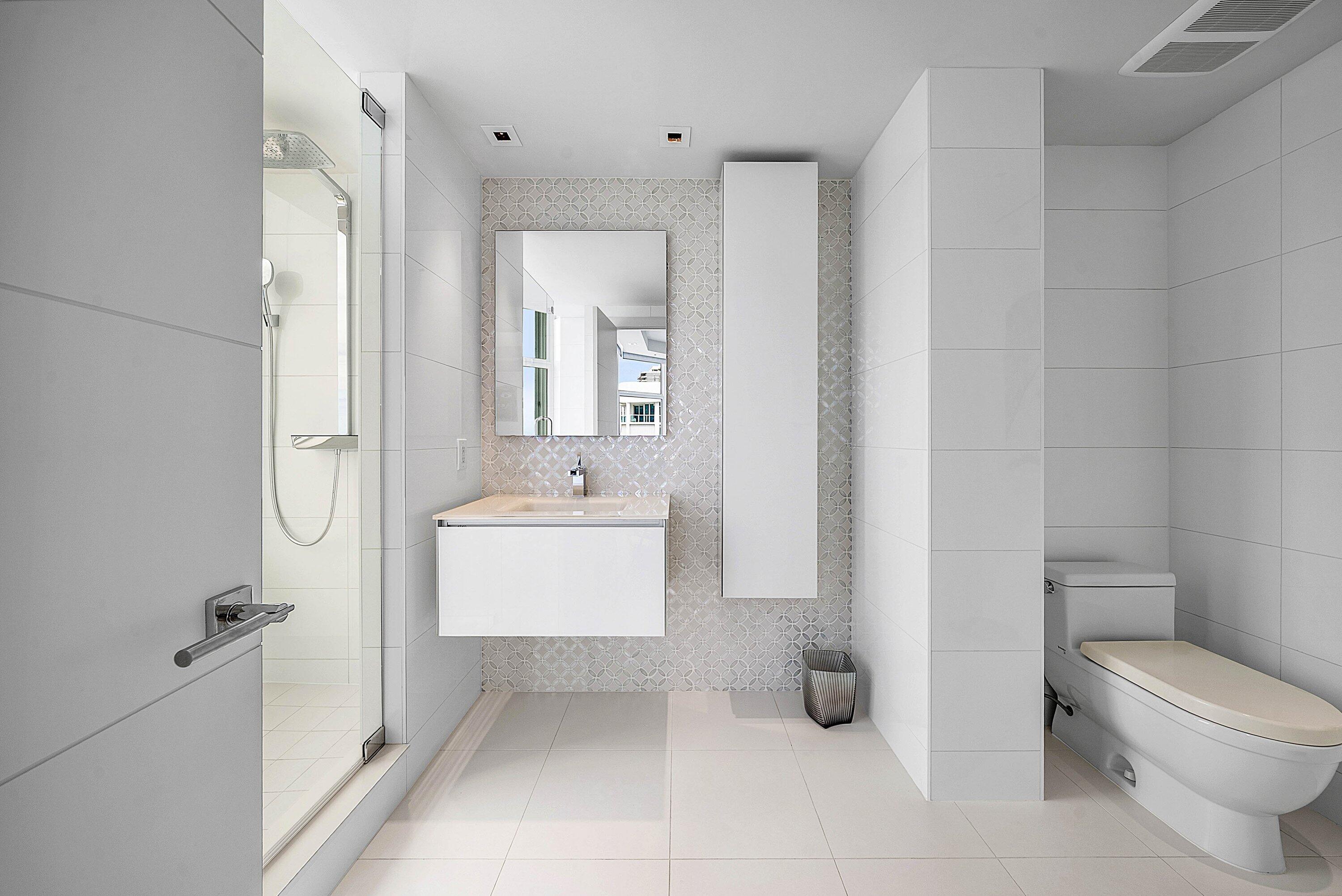 Modern bathroom featuring a glass-enclosed shower, wall-mounted floating vanity, integrated rectangular sink, full-height decorative tile backsplash, and floor-to-ceiling storage cabinetry