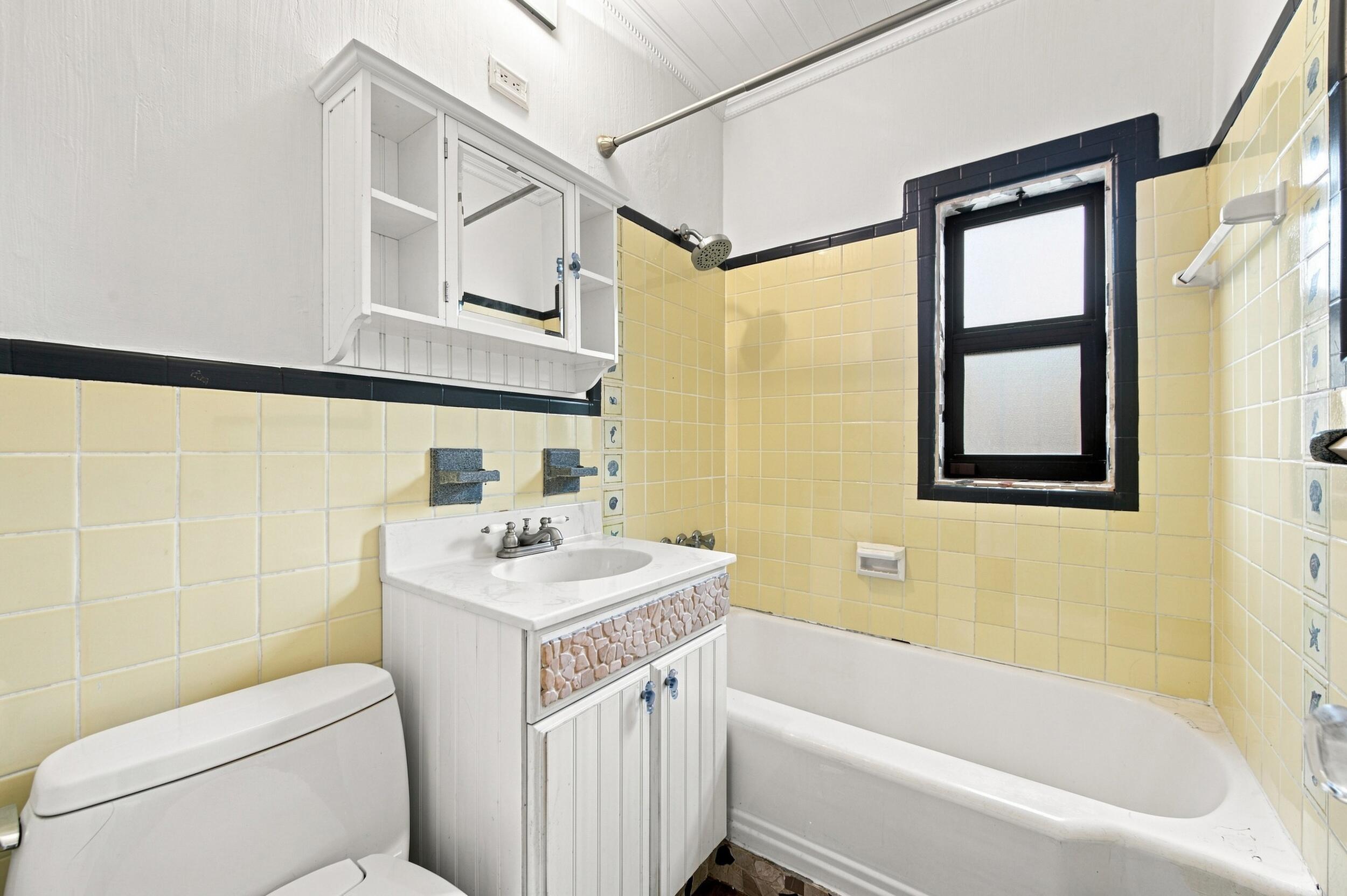 Bathroom featuring a white vanity with decorative stone inlay, wall-mounted medicine cabinet, bathtub with shower fixture, and yellow ceramic wall tiling with black accent trim