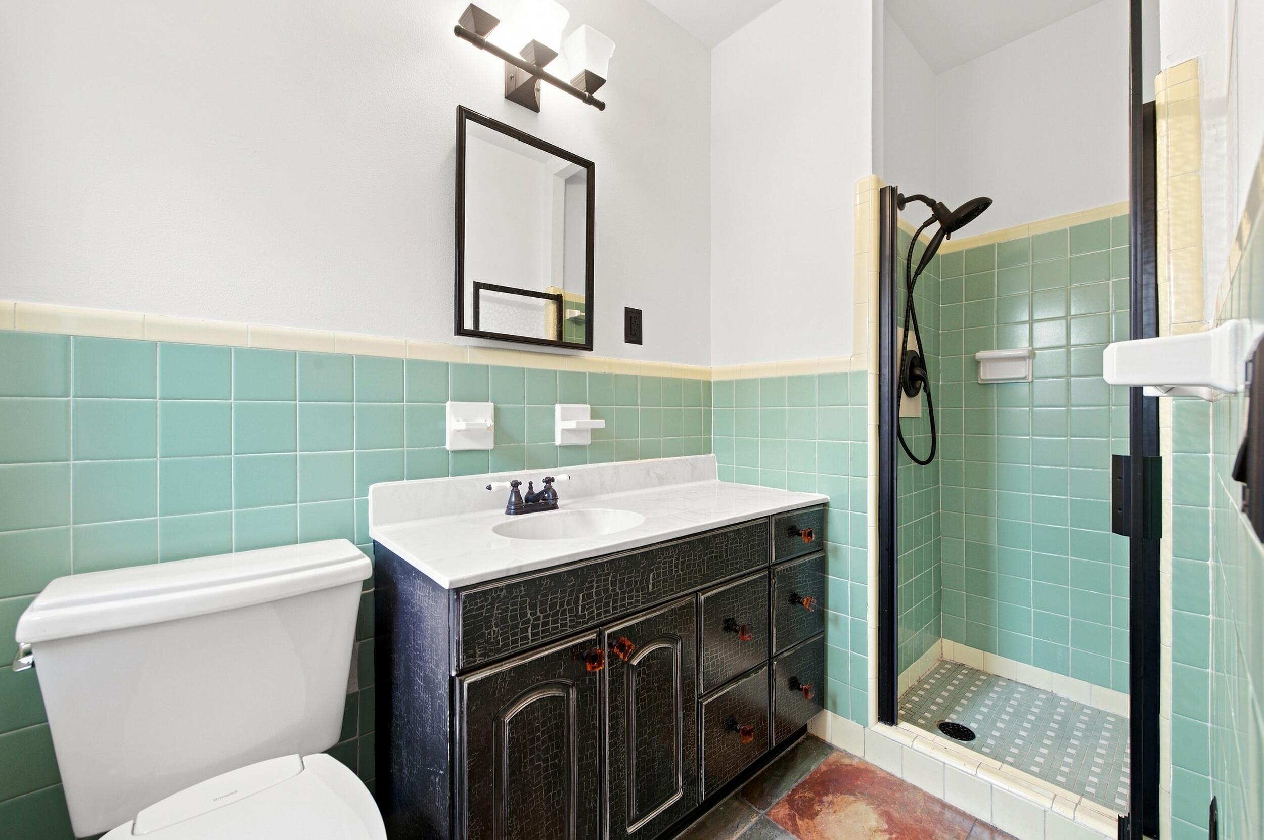 Bathroom featuring a vanity with a white countertop and oval under-mount sink, matte black hardware, a tiled shower enclosure, and a rectangular wall mirror