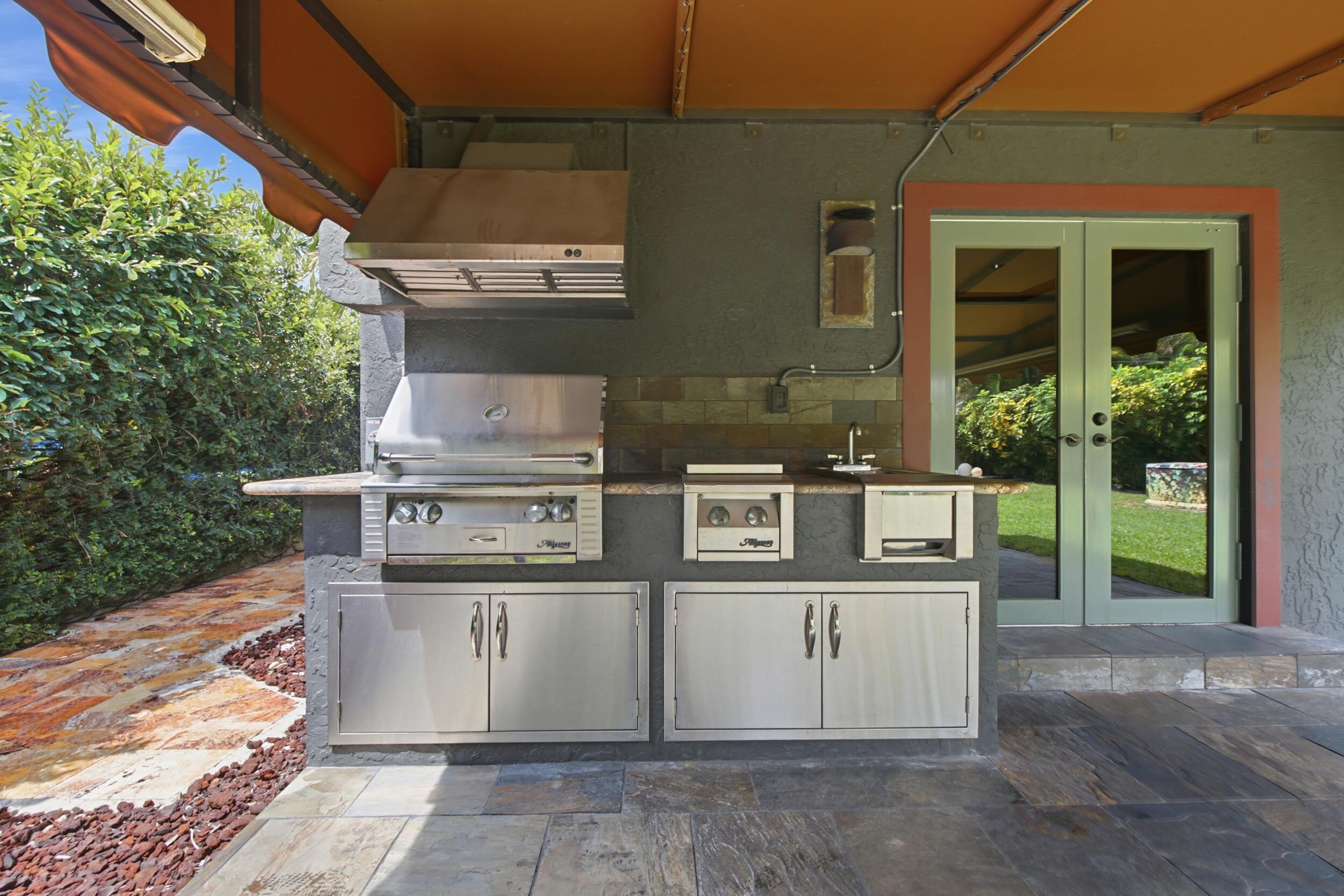 Outdoor kitchen featuring stainless steel built-in grill, dual-burner cooktop, integrated sink, stone countertop, and stainless steel cabinetry under a covered patio