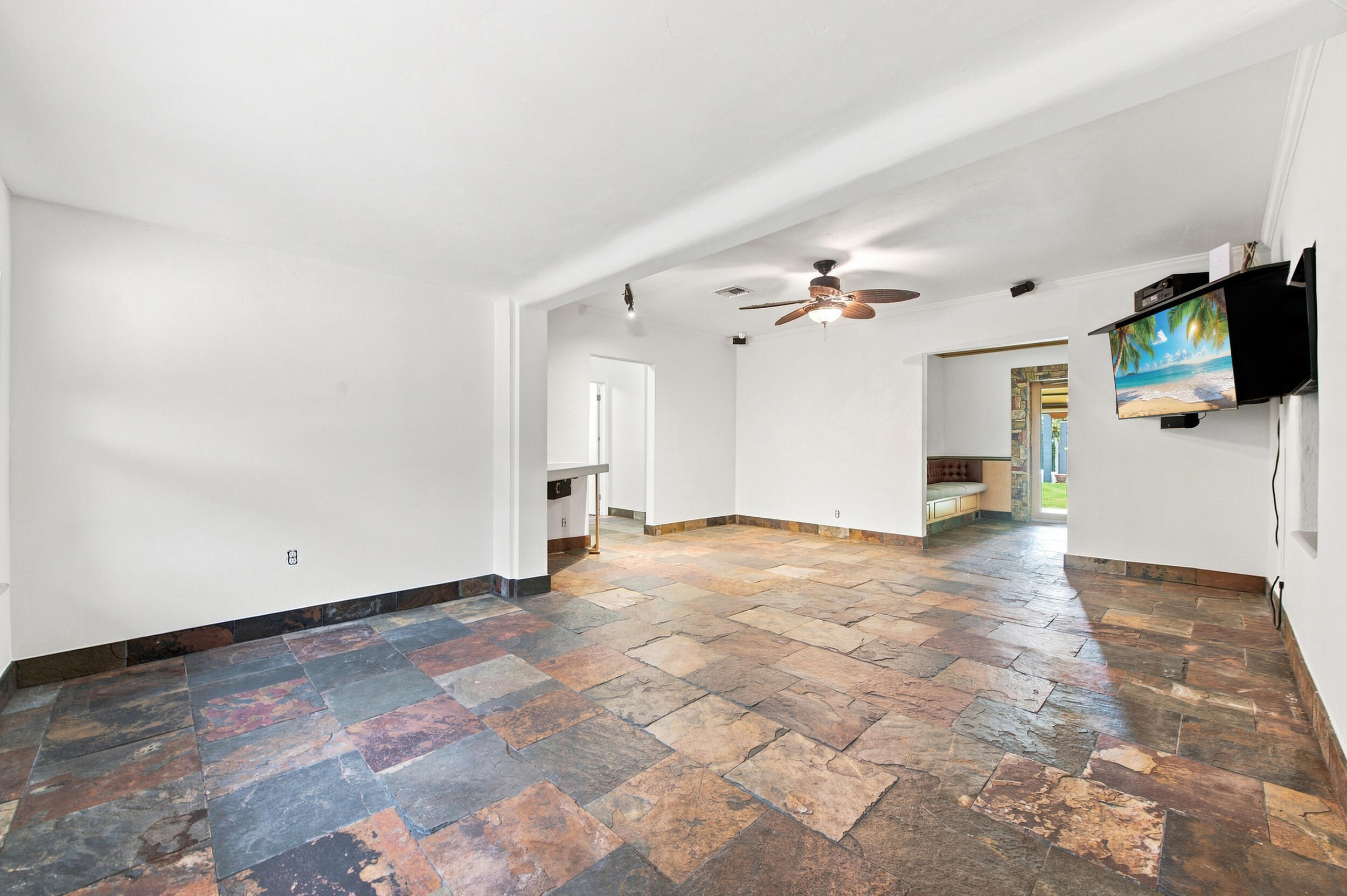 Interior space featuring multi-tonal natural stone flooring, a central ceiling fan with integrated lighting, built-in recessed wall shelving, and a stone-framed entryway