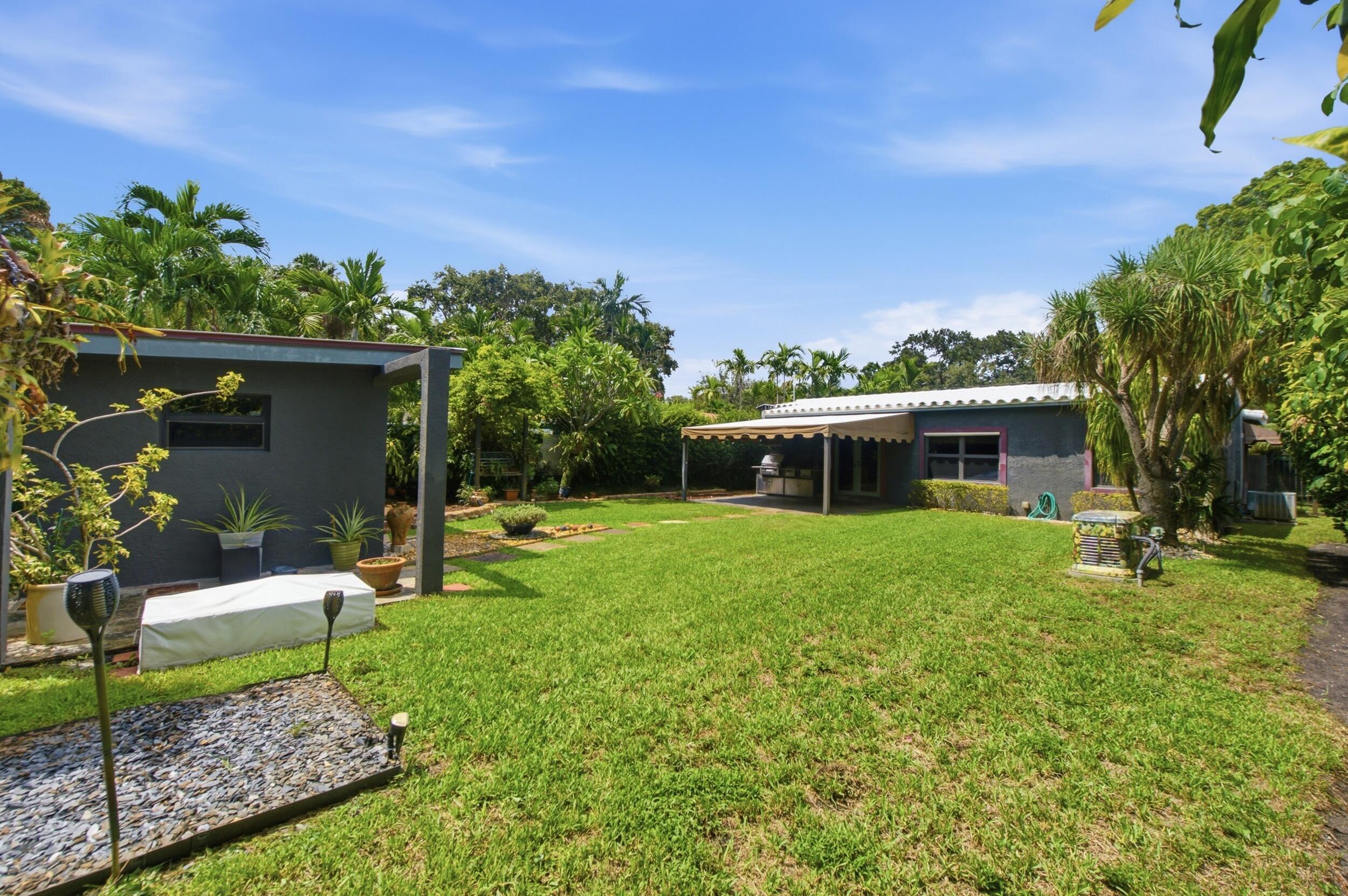 Expansive backyard featuring a manicured lawn, detached structure, covered patio, mature landscaping, and hardscaped garden beds